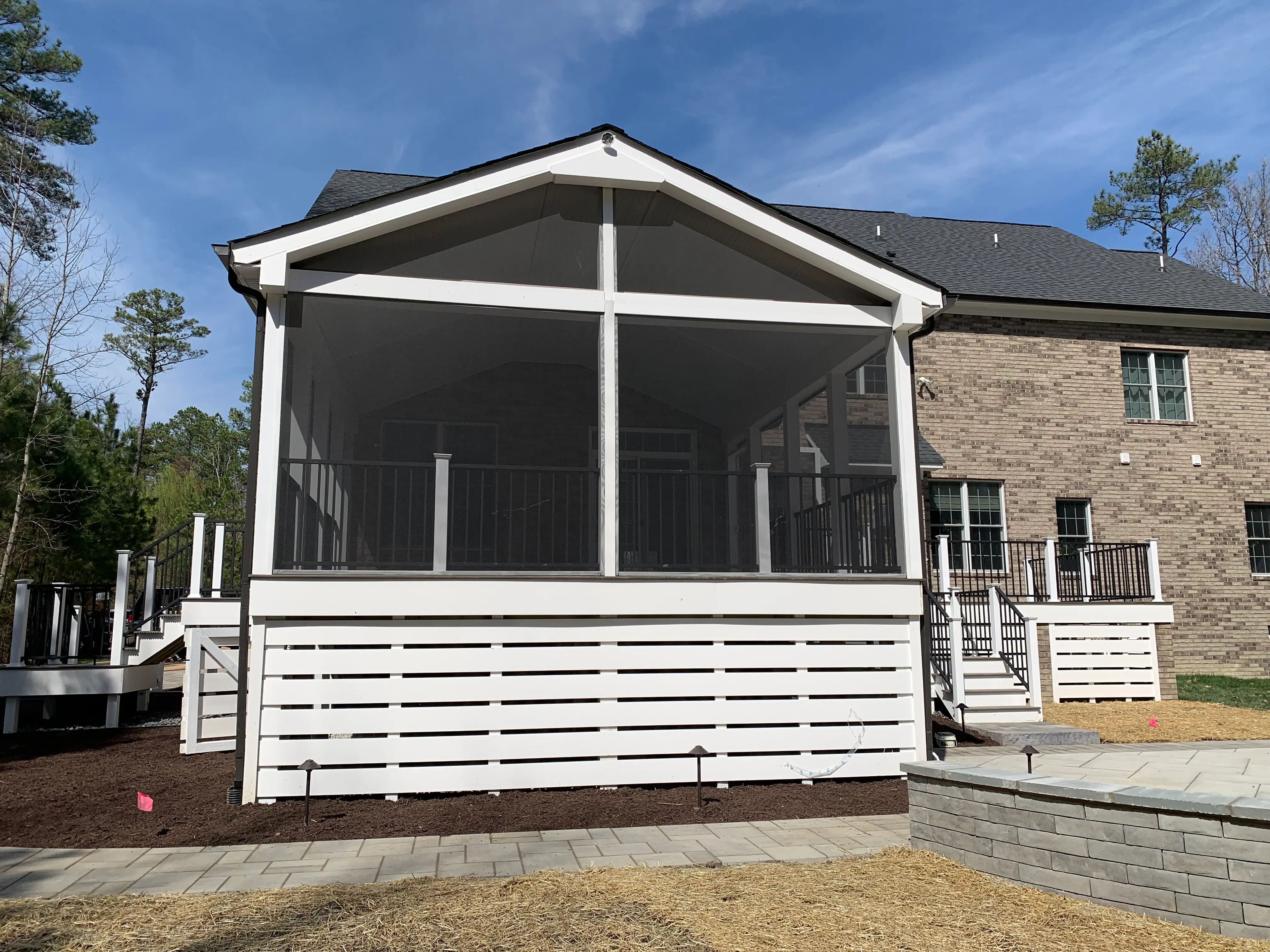 Large screen porch with deck made of Trex Coastal Bluff and stairs leading to back yard with a large stone patio and stairs on the other side of the porch, leading to the driveway on the side of the house