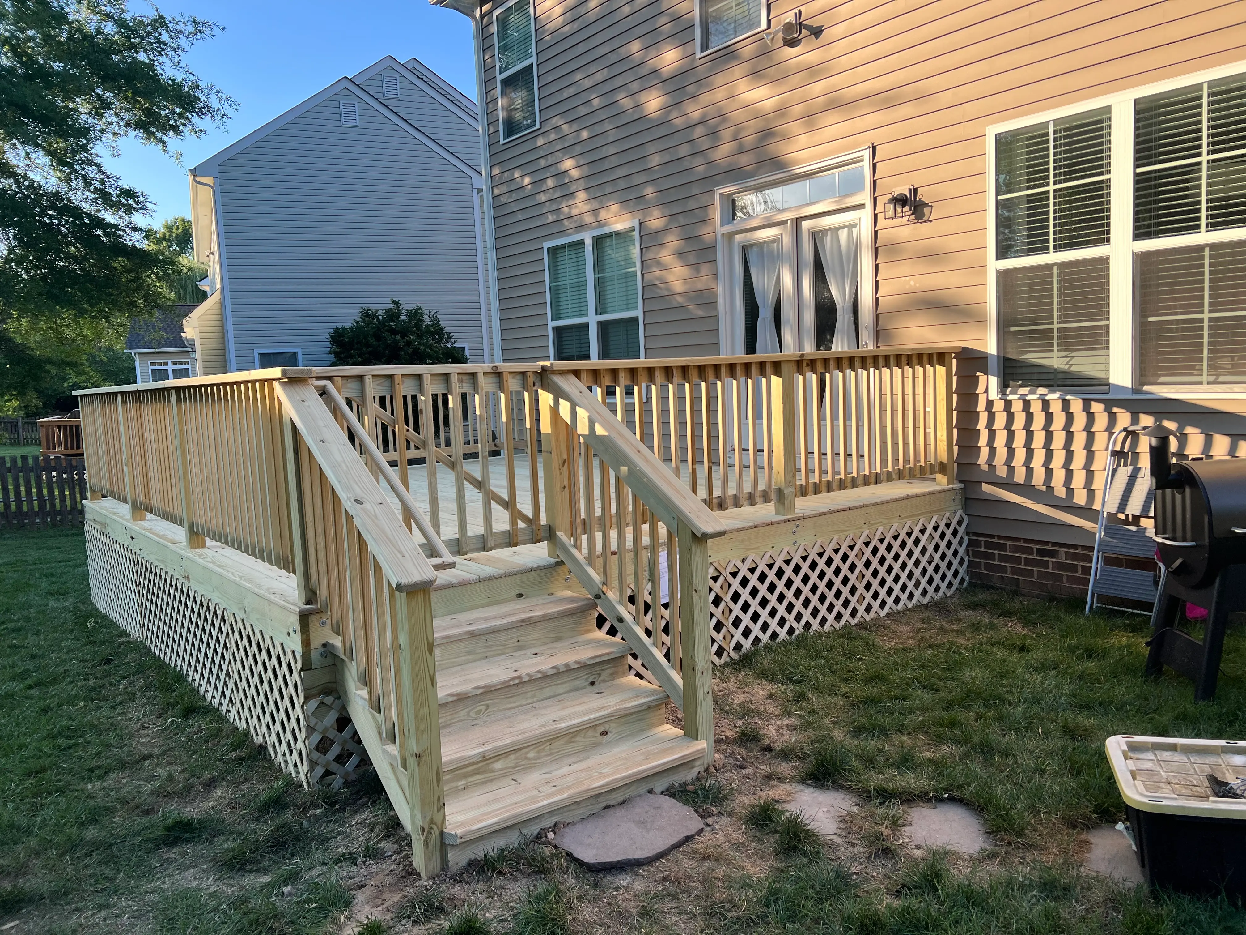 A clean wood deck with a gate by the stairs leading into the backyard, with simple crossing lattice