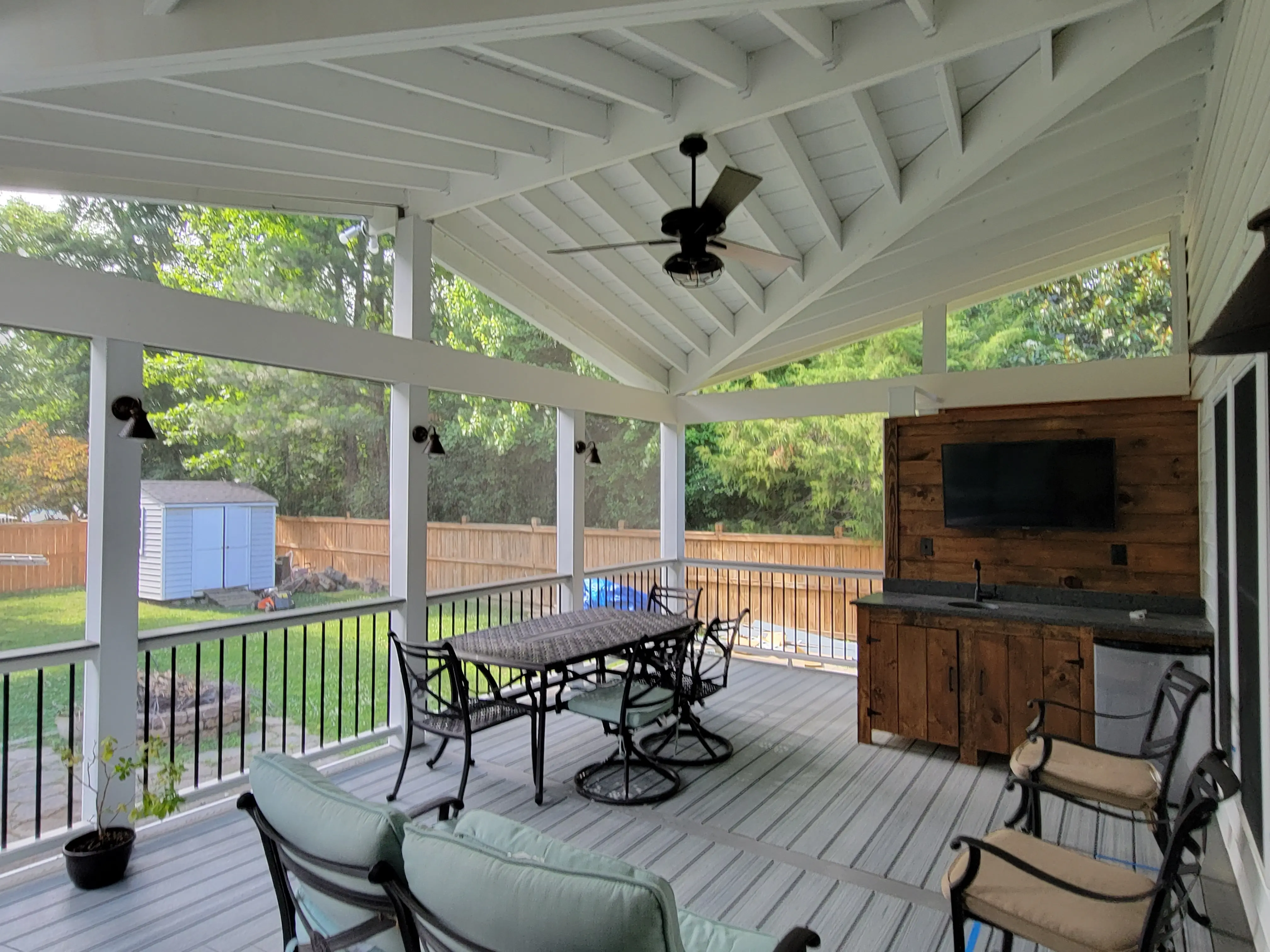 Spacious screened porch with a vaulted ceiling, featuring a dining table with chairs, a couch, and a wall-mounted TV.