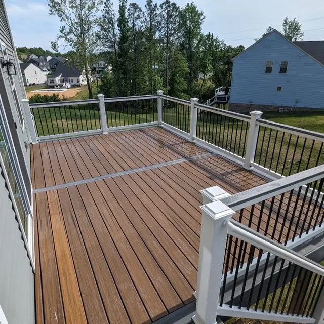 Decking with Long Staircase project after completion; A deck with a large staircase with white railings with black balusters leading down to a grassy yard. The decking is made of Trex Island Mist and Havana Gold.