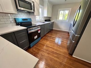 A renovated kitched featuring white countertops, above grey cabinets, and white cabinets over the counter. The backsplash is white subway tile