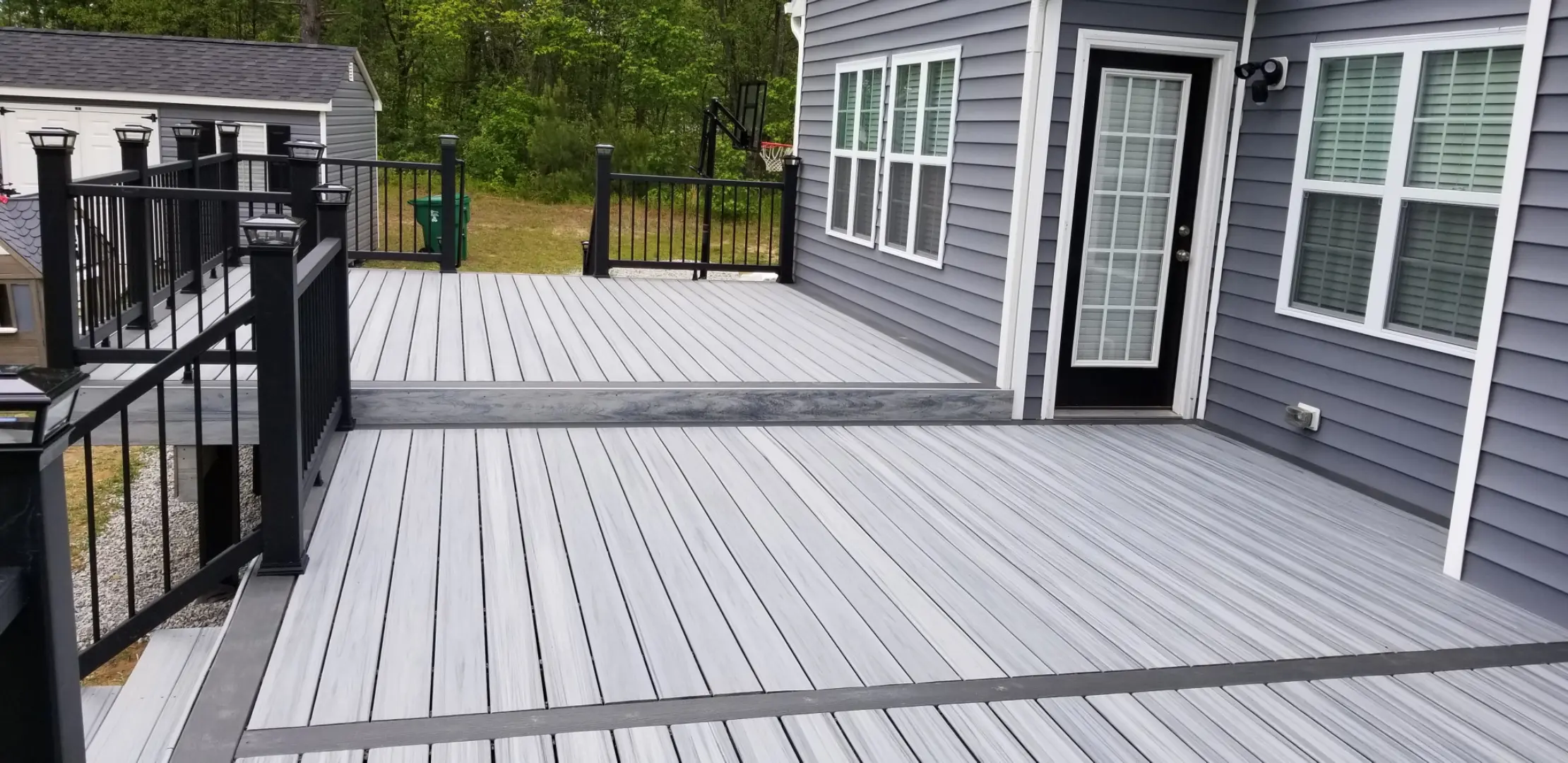 Spacious wooden deck with Trex Foggy Wharf boards attached to a house, featuring black railings and steps leading down to the backyard.