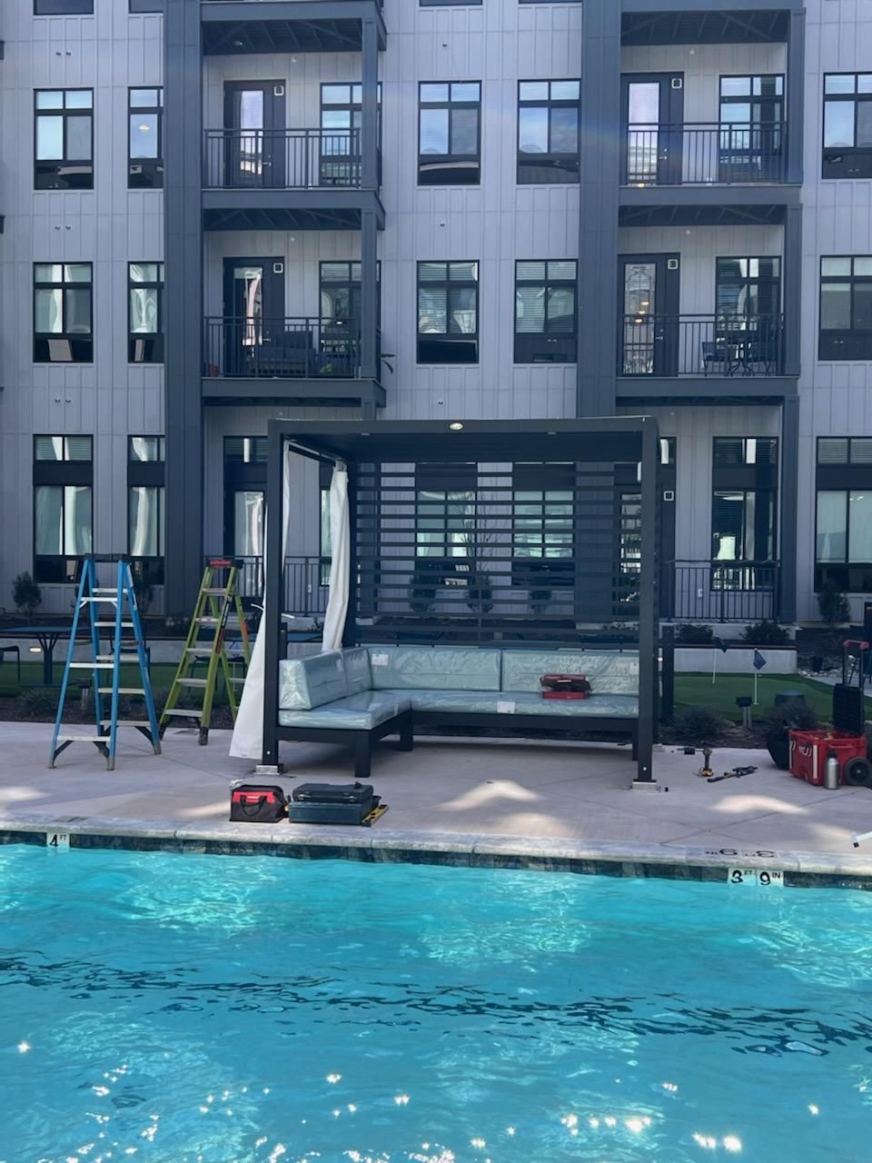 A black gazeba with attached benches, poolside in an apartment community