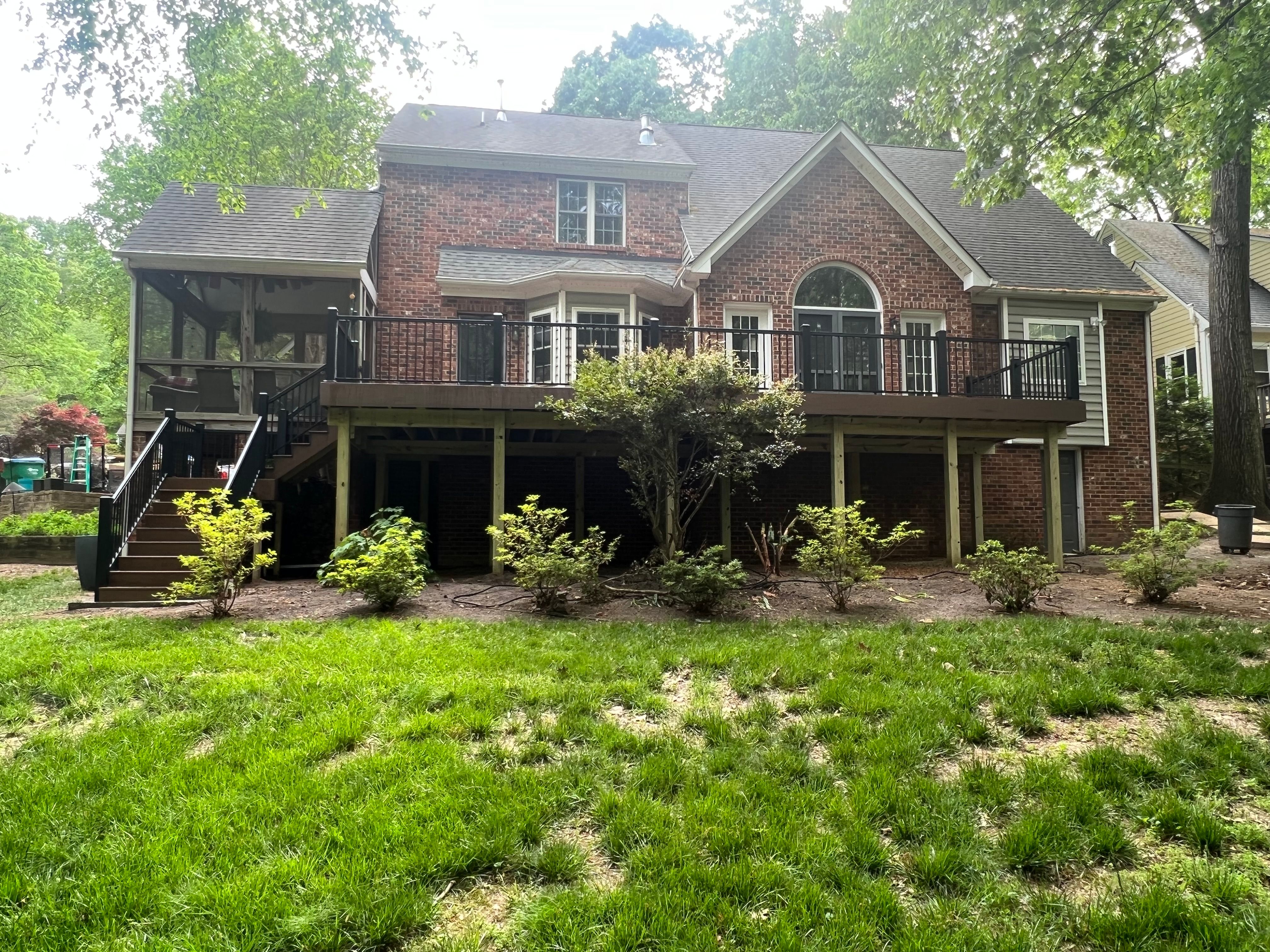 A large deck made of TimberTech Terrain Brown Oak composite decking with black aluminum railings attached to a brick house with stairs leading into the backyard