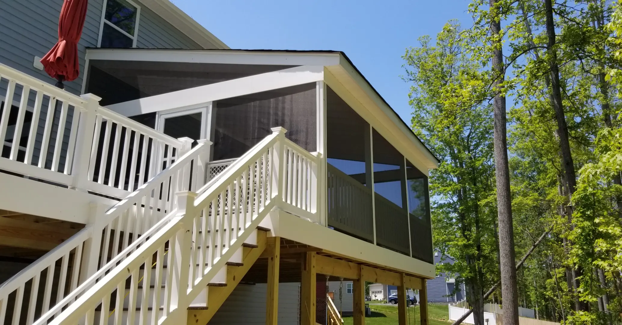 A large screened porch is attached to the second floor of a house with white railings and stairs leading down to a grassy yard