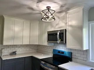 A renovated kitchen with white cabinets over a white countertop over grey cabinets. The backsplash is a white subway tile.