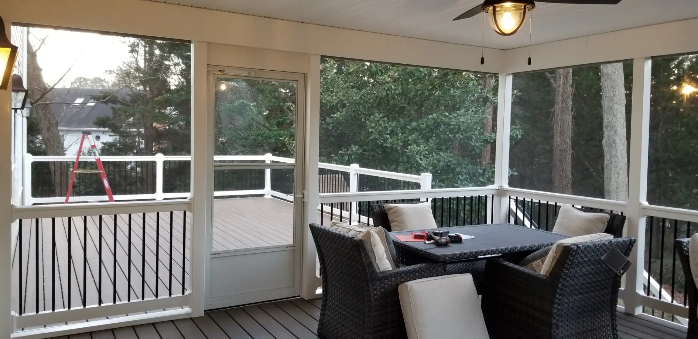 Screen porch made of Trex Toasted Sand composite decking. Door leads to an outdoor deck with white railing with black balusters.
