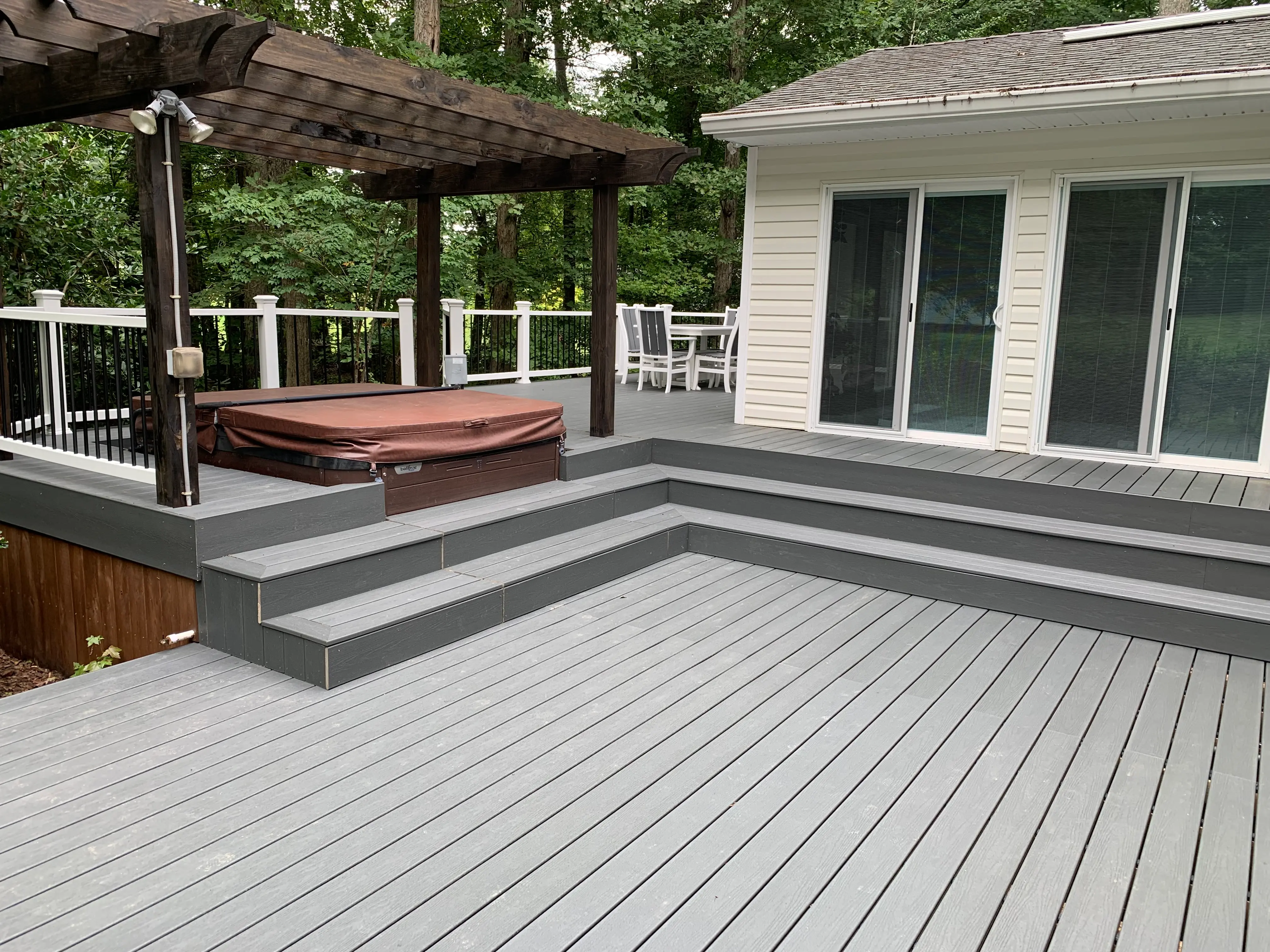 A large grey deck made of Trex Clamshell decking, with a dark brown pergola over a hottub inside of the deck