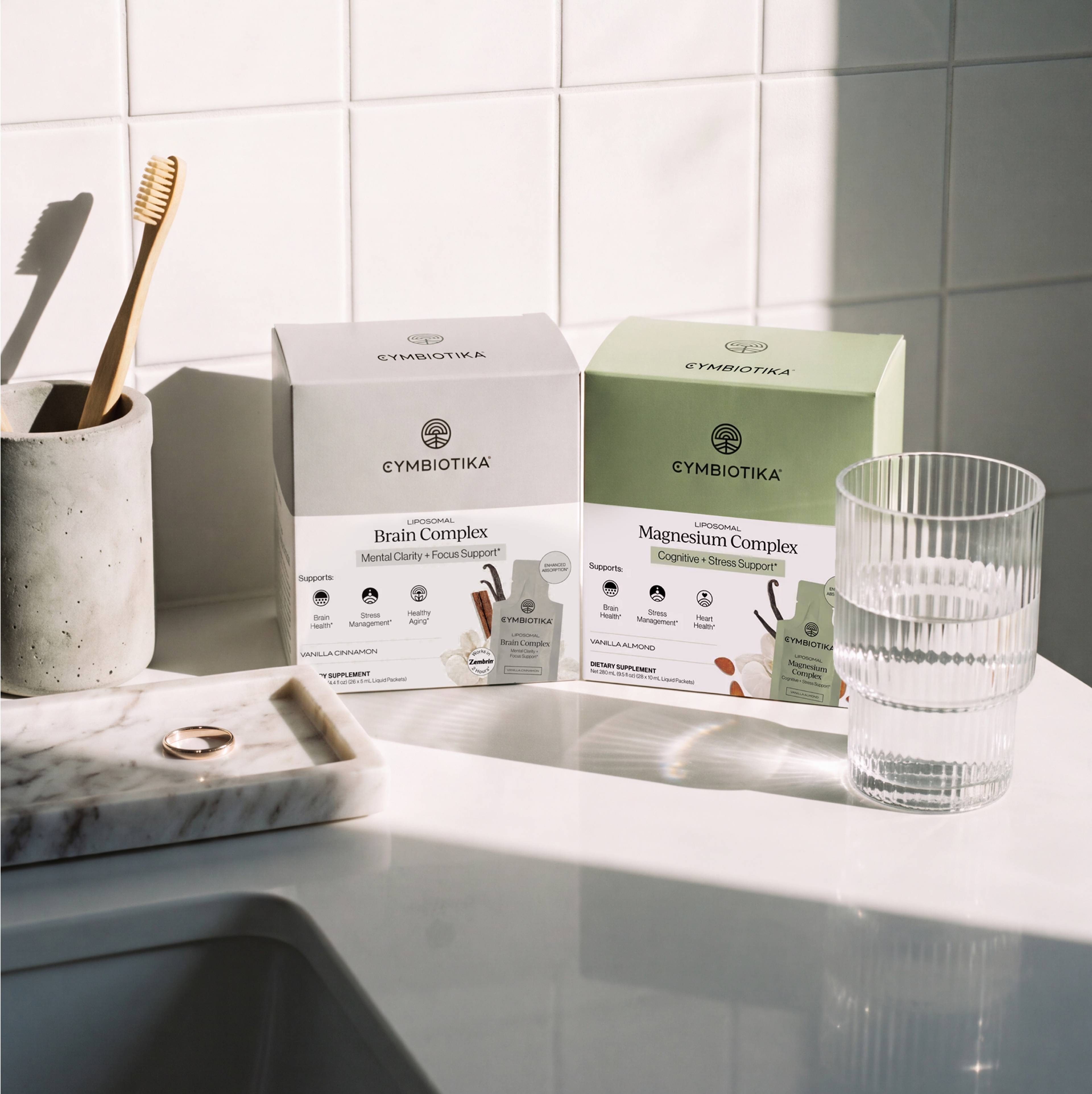 Liposomal Brain Complex and Liposomal Magnesium Complex boxes displayed beside a toothbrush holder and drinking glass.
