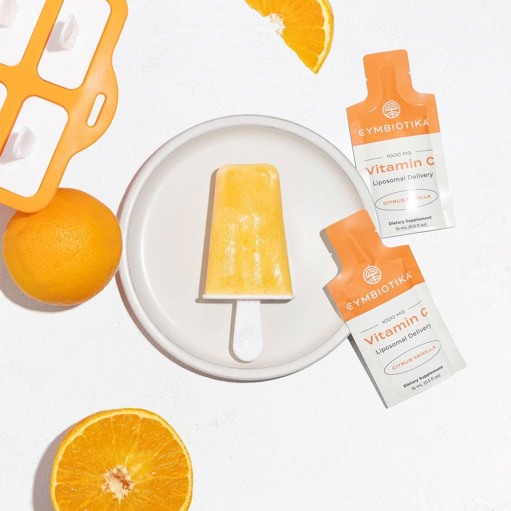 Orange creamsicle on a plate with oranges, a popsicle mold, and Cymbiotika Liposomal Vitamin C packets.