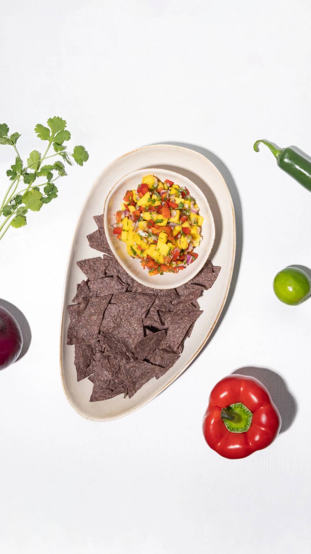 Bowl of mango salsa with blue corn tortilla chips, cilantro, lime, jalapeño, and red bell pepper.