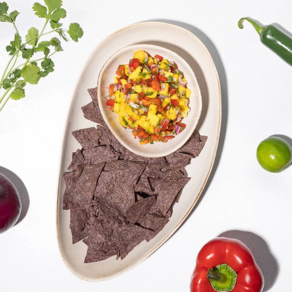 Bowl of mango salsa with blue corn tortilla chips, cilantro, lime, jalapeño, and red bell pepper.