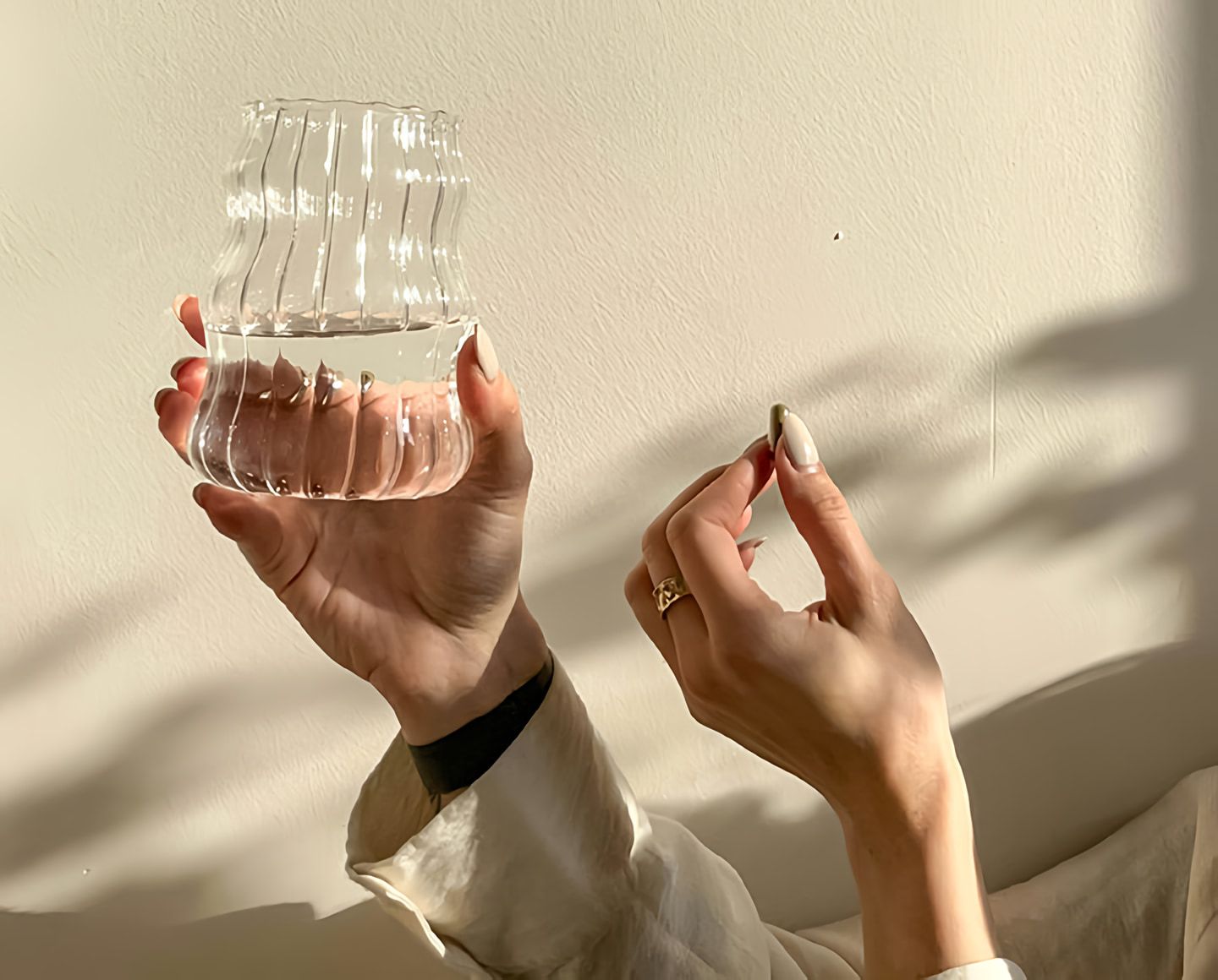 Hands holding a ribbed transparent vessel of water and a small oblong object in warm sunlight.
