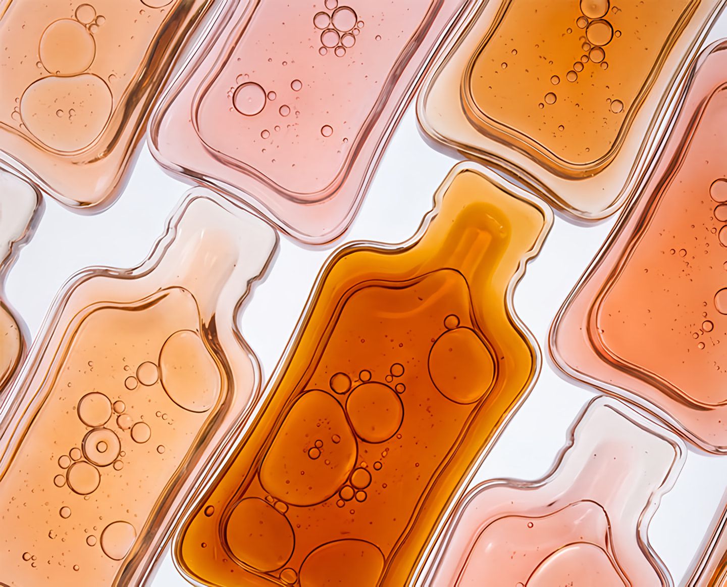 Overlapping translucent rounded shapes filled with amber, peach, and pink liquid, with air bubbles.