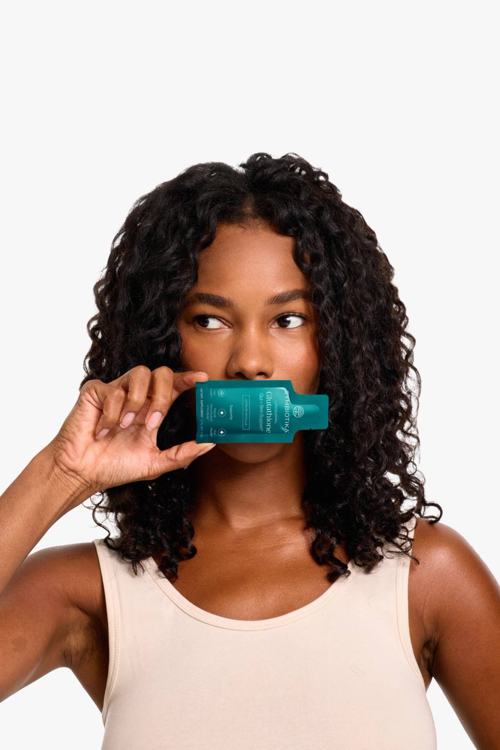 Woman holding a Cymbiotika Liposomal Glutathione packet beneath her nose against a white background.