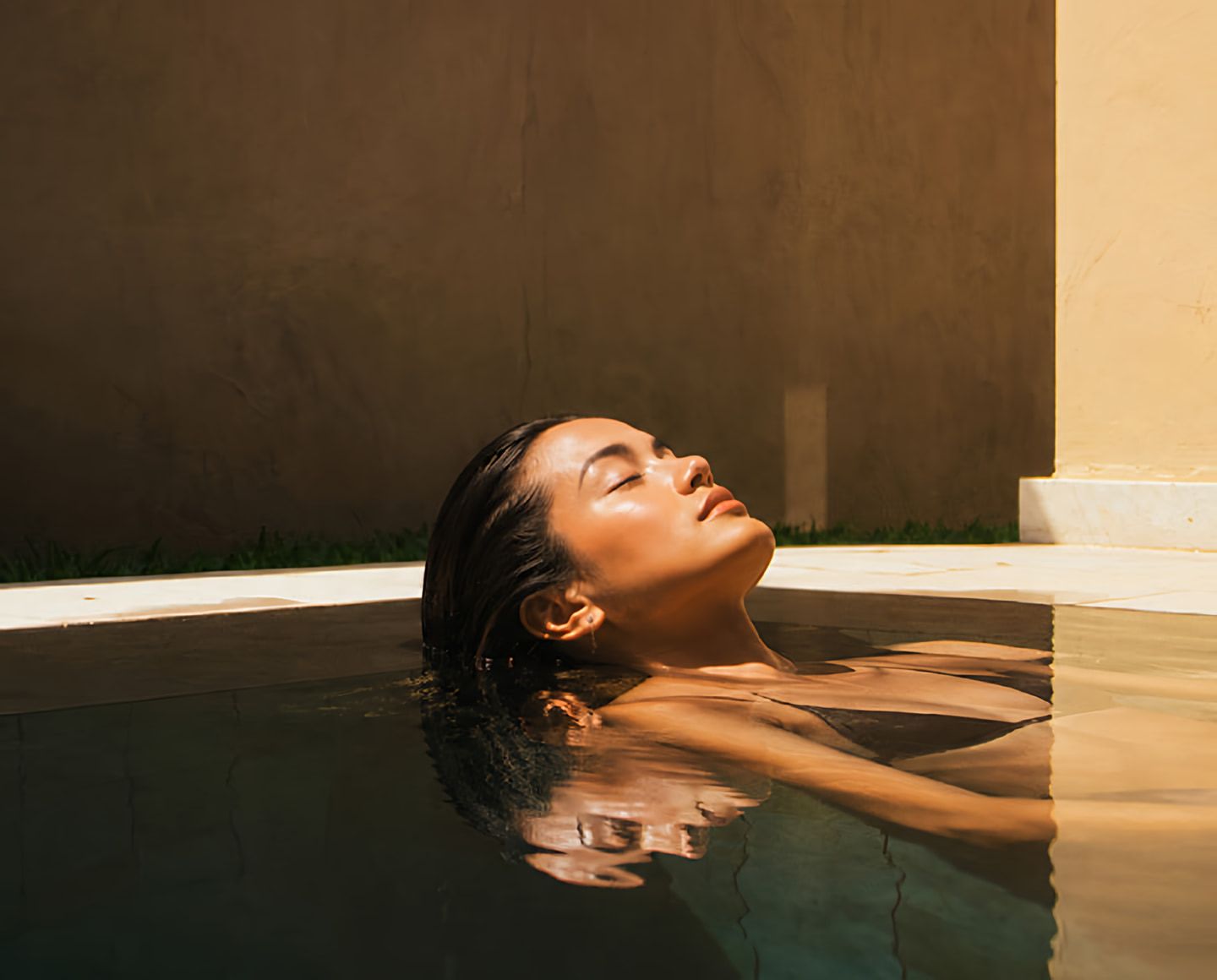 Woman floating peacefully in a sunlit pool with her eyes closed.