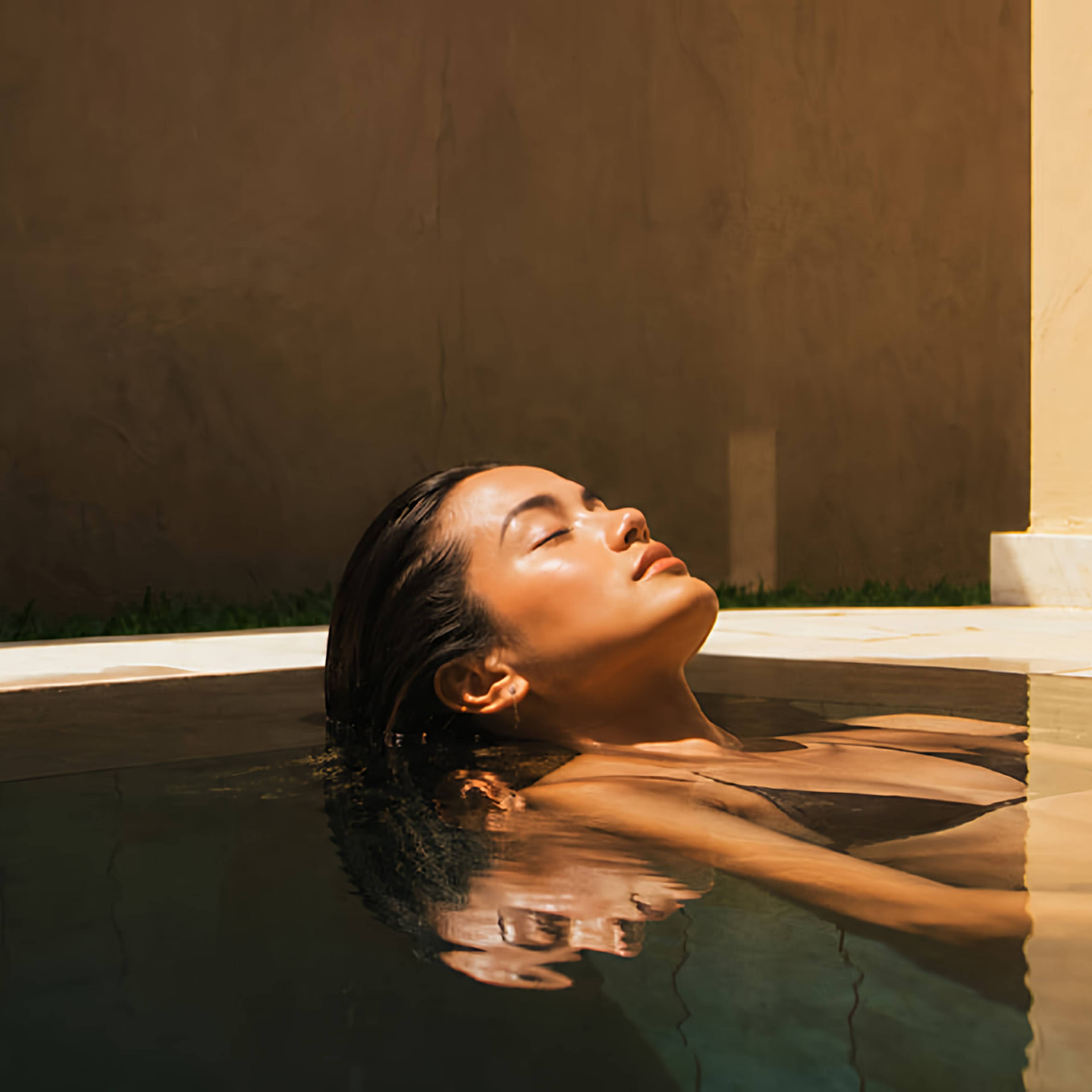 Woman floating peacefully in a sunlit pool with her eyes closed.