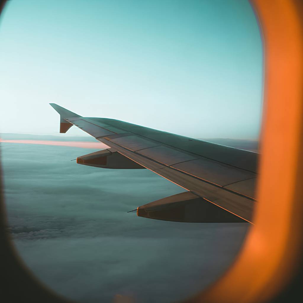 Airplane wing seen through a window above a layer of clouds.