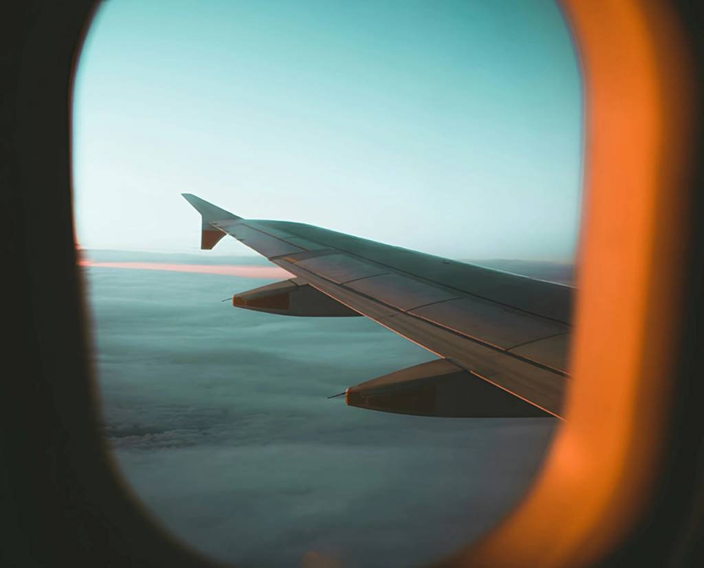 Airplane wing seen through a window above a layer of clouds.