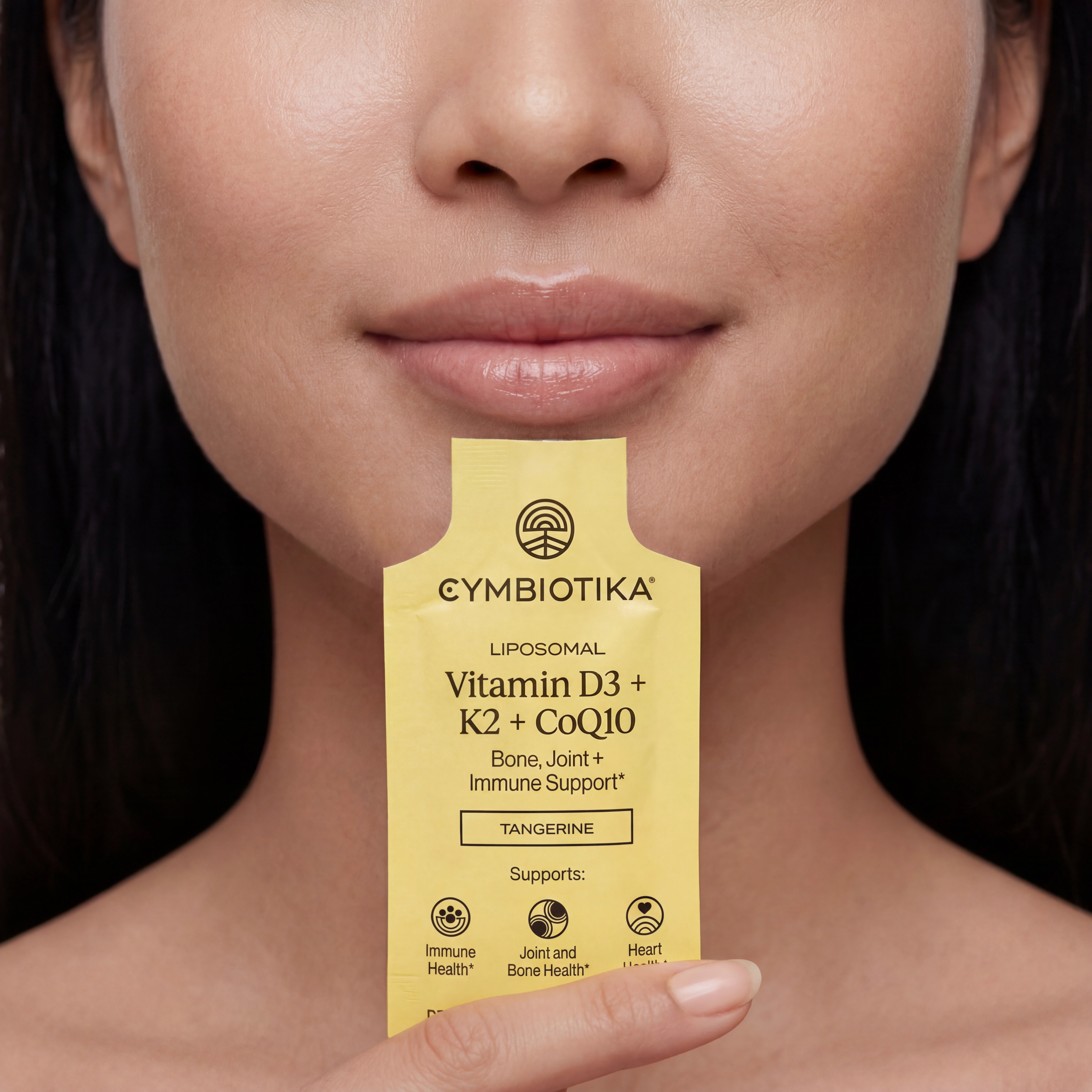 Person holds a yellow Liposomal Vitamin D3 + K2 + CoQ10 sachet below their lips.
