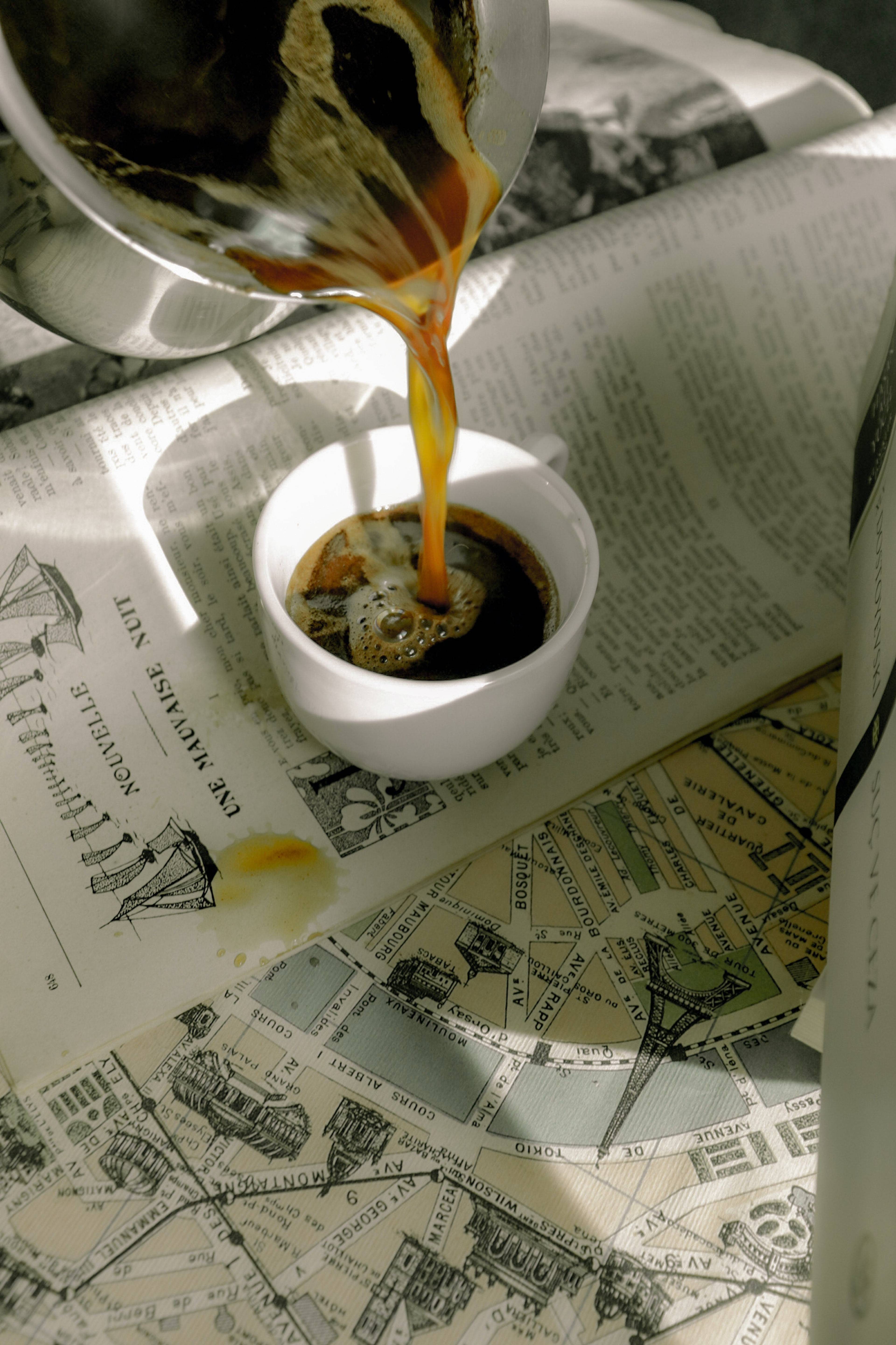 Coffee being poured from a glass carafe into a white cup on open illustrated pages.