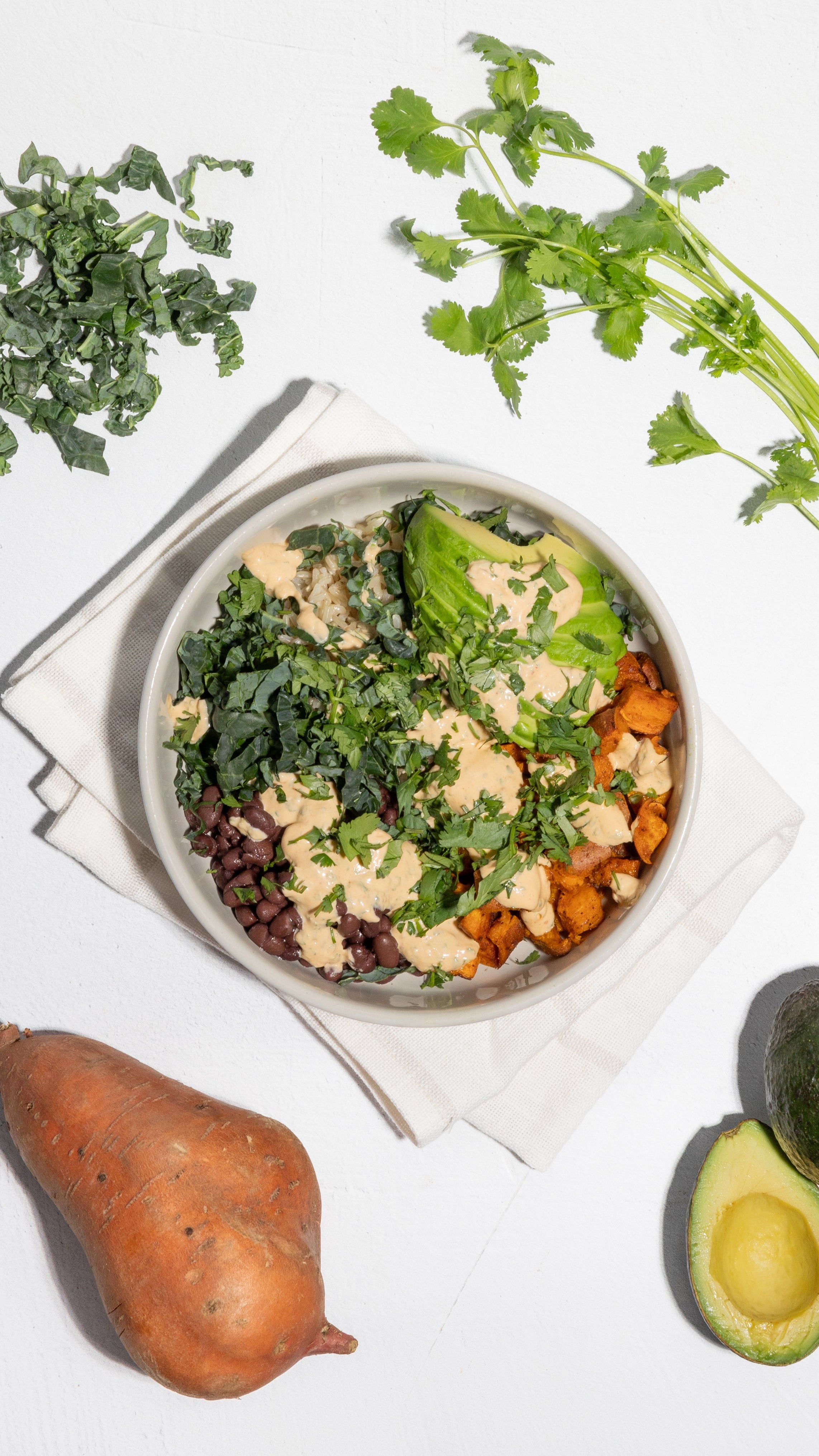Buddha bowl with sweet potatoes, black beans, kale, avocado, grains, and creamy dressing.