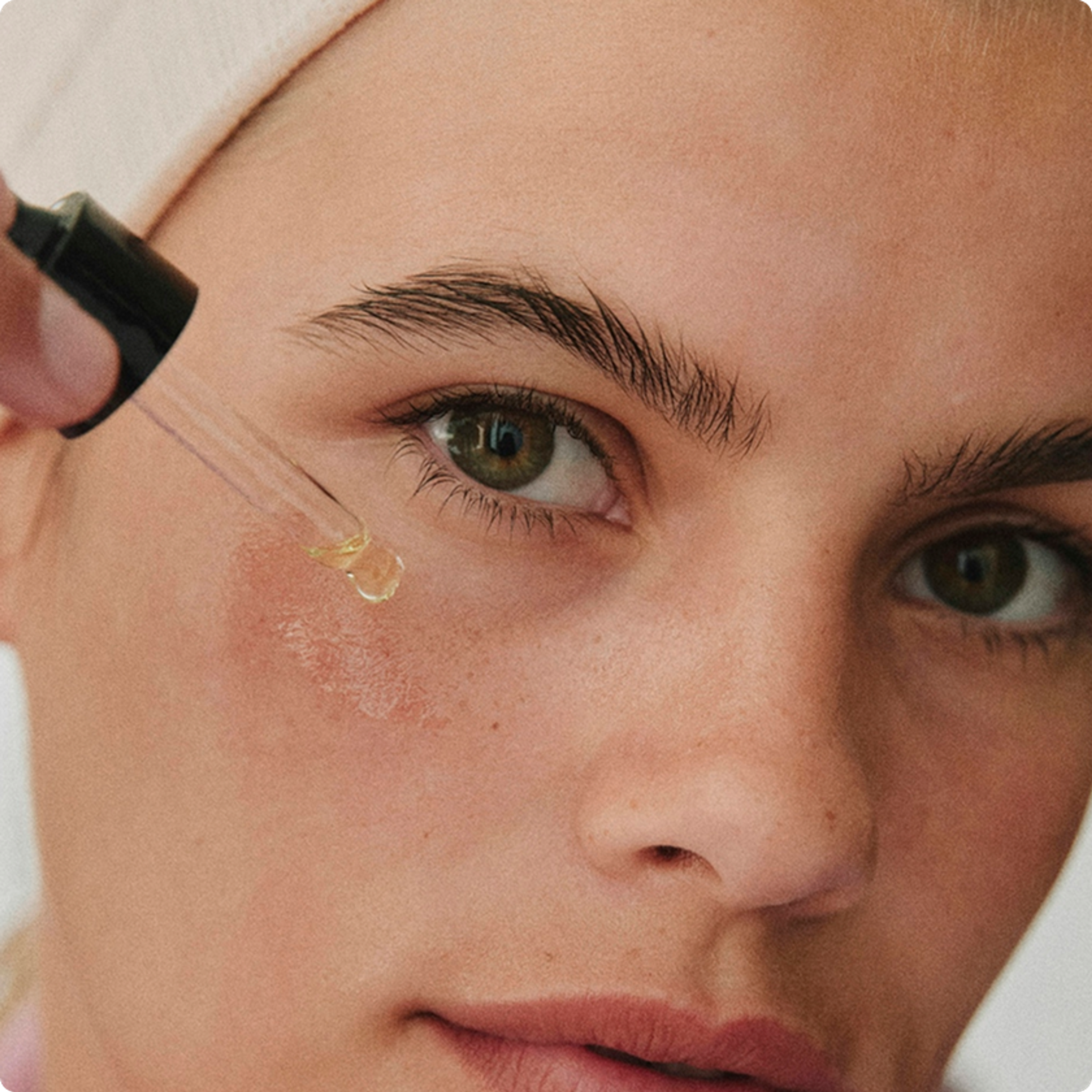 Close-up of a person applying a drop of serum to the skin beneath their eye with a dropper.