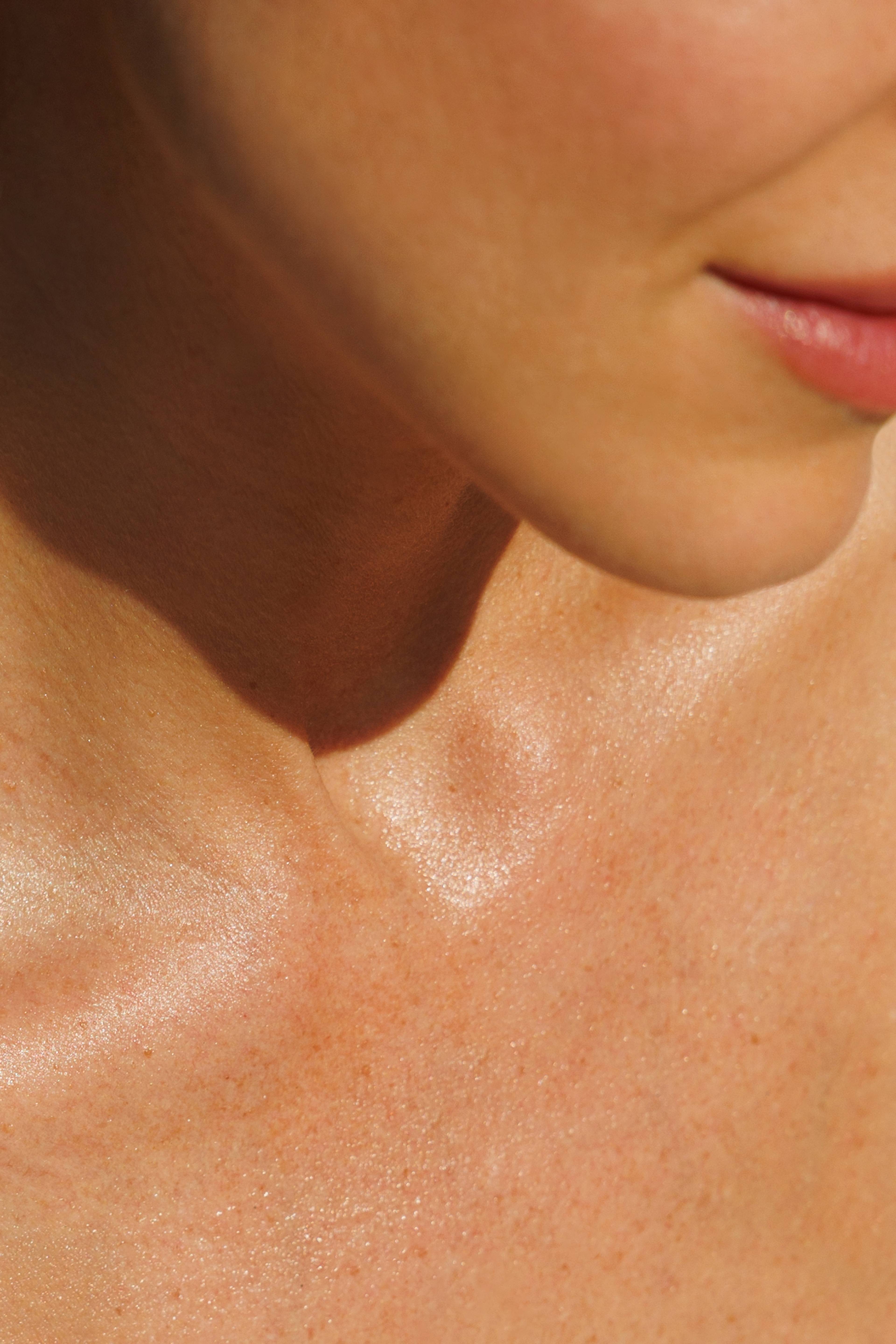 Close-up of a person's lower face, neck, and collarbone in warm sunlight, with skin visibly glowing.