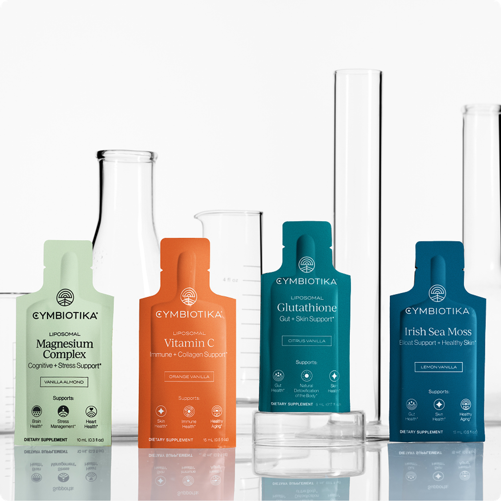 Four Cymbiotika supplement pouches—Magnesium Complex, Vitamin C, Glutathione, and Irish Sea Moss—arranged before laboratory glassware.