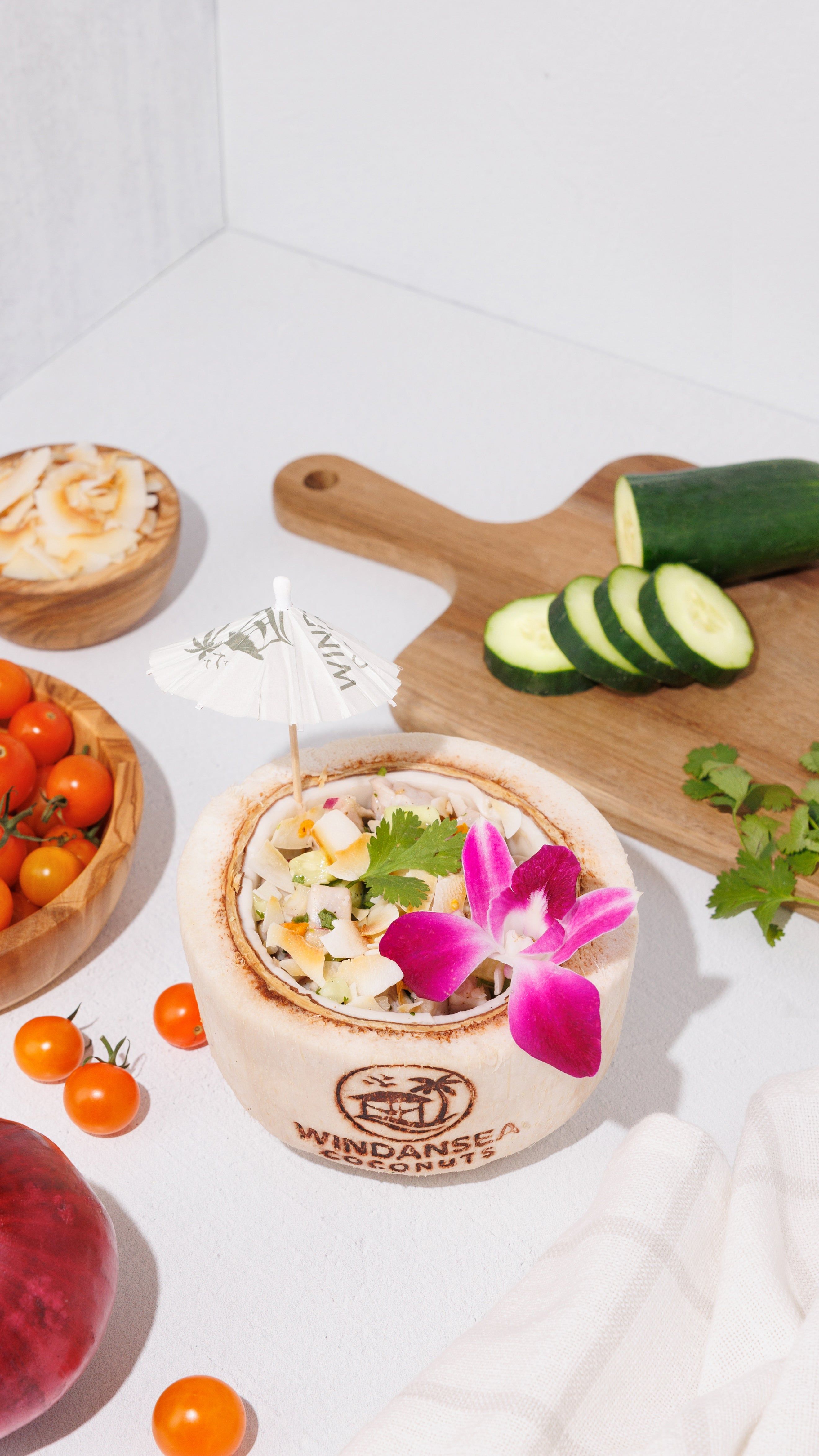 Ceviche served in a branded coconut shell with cucumber, cherry tomatoes, cilantro, and a pink orchid.