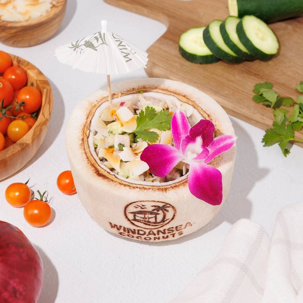 Ceviche served in a branded coconut shell with cucumber, cherry tomatoes, cilantro, and a pink orchid.