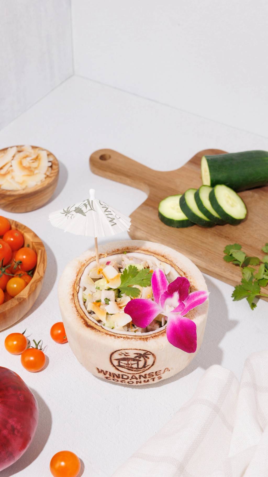 Ceviche served in a branded coconut shell with cucumber, cherry tomatoes, cilantro, and a pink orchid.
