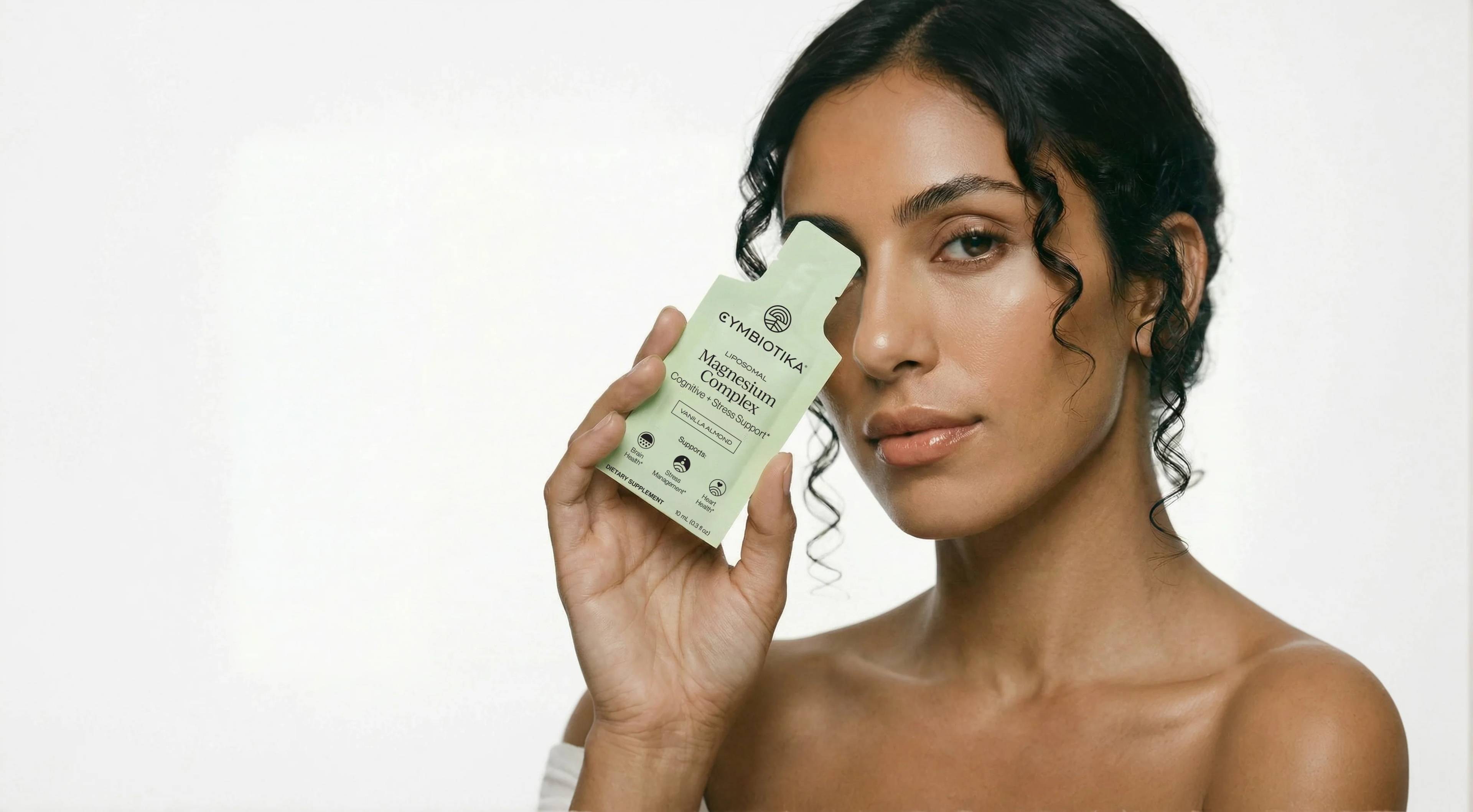 Woman holding a box of Cymbiotika Liposomal Magnesium Complex beside her face.