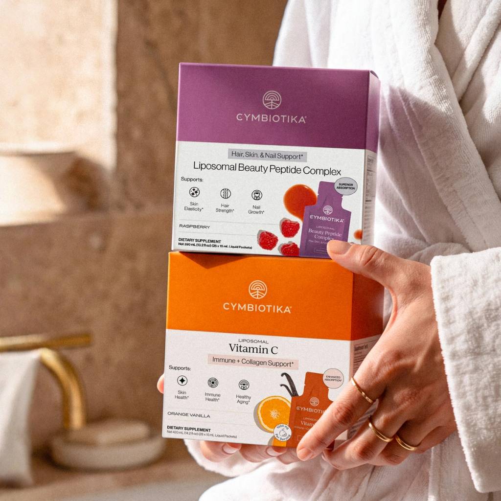 A person in a white robe holds boxes of Liposomal Beauty Peptide Complex and Liposomal Vitamin C.