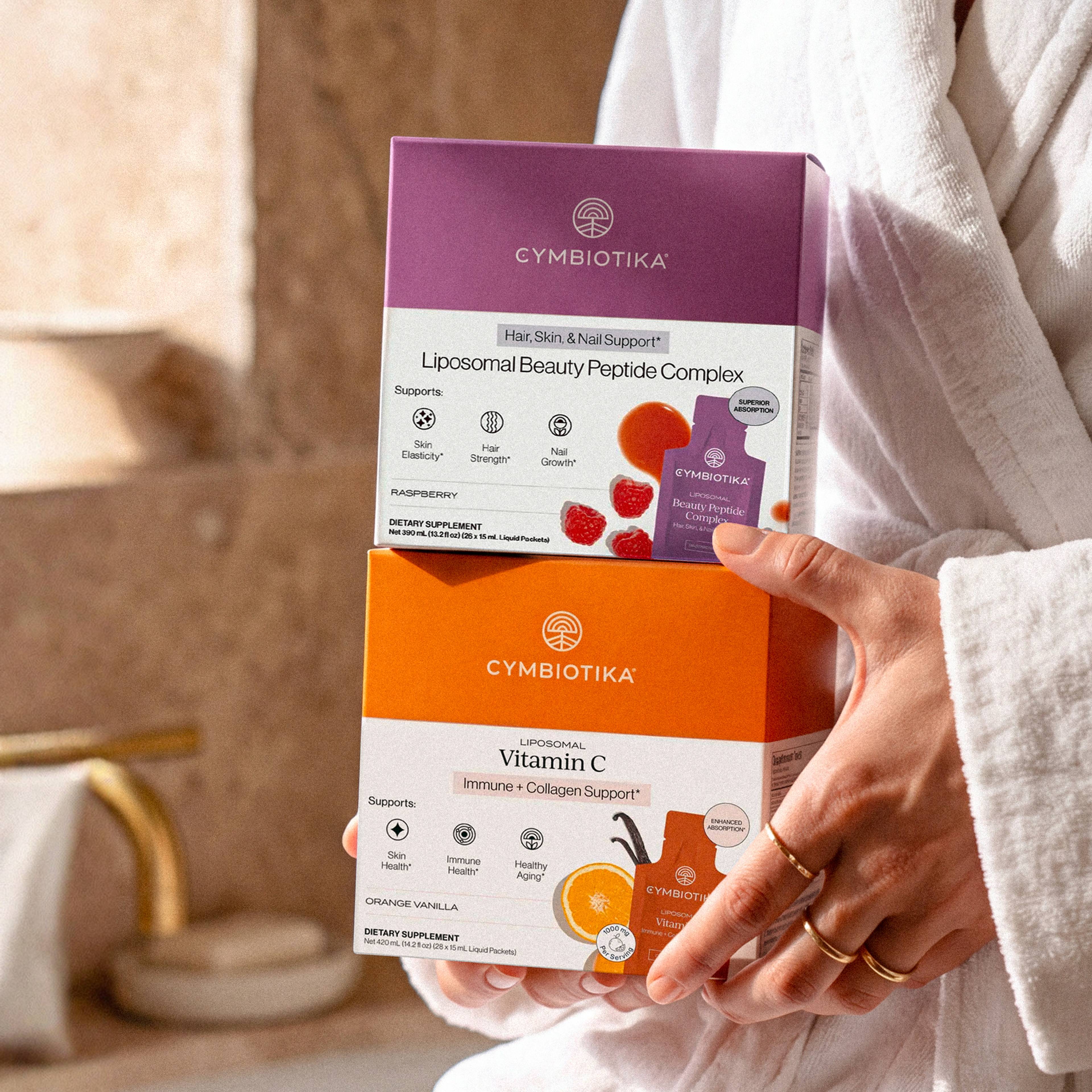 A person in a white robe holds boxes of Liposomal Beauty Peptide Complex and Liposomal Vitamin C.