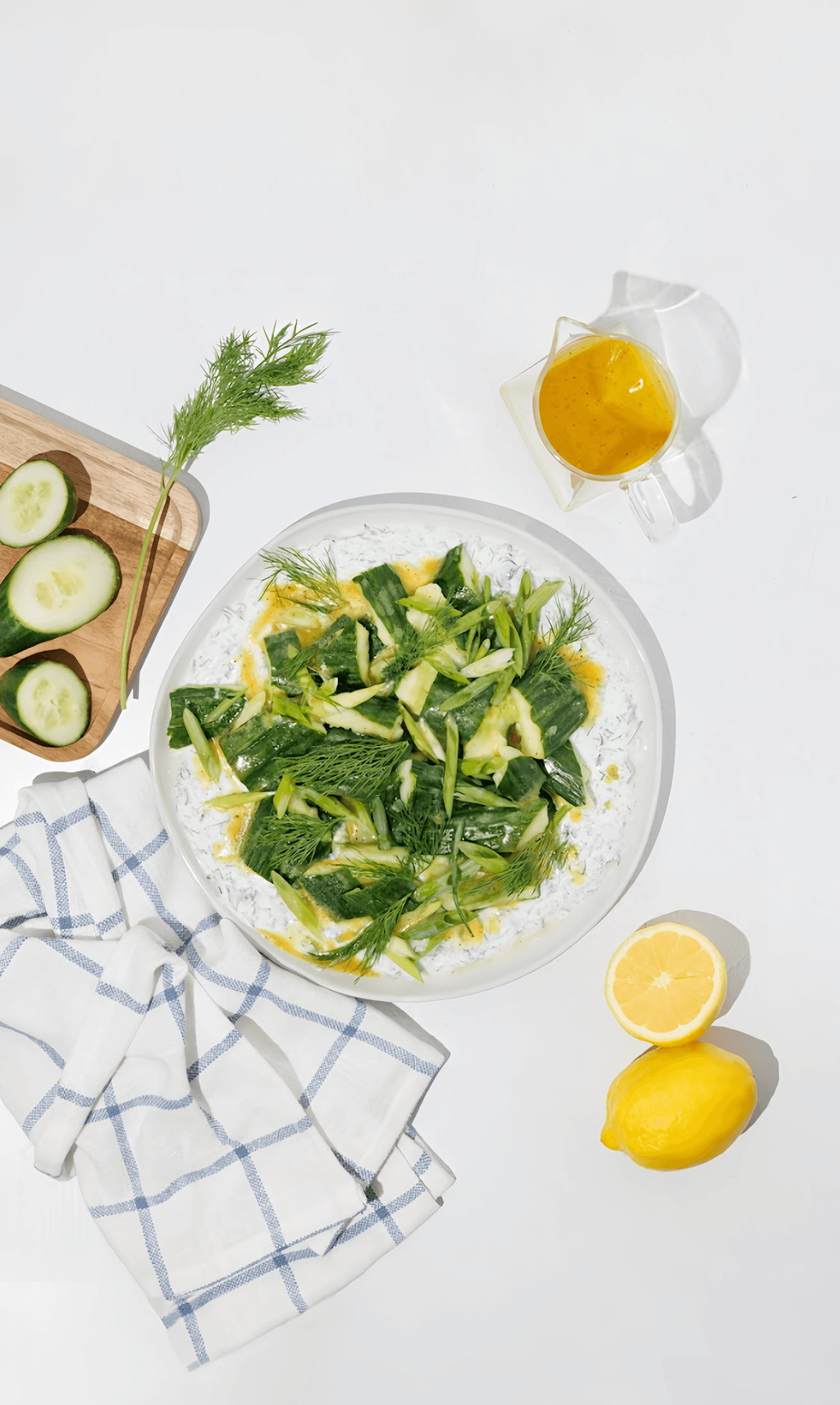 Cucumber salad with dill and yellow dressing on a yogurt-covered plate, with lemon and sliced cucumber.