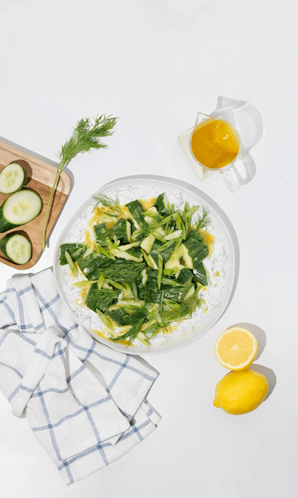 Cucumber salad with dill and yellow dressing on a yogurt-covered plate, with lemon and sliced cucumber.