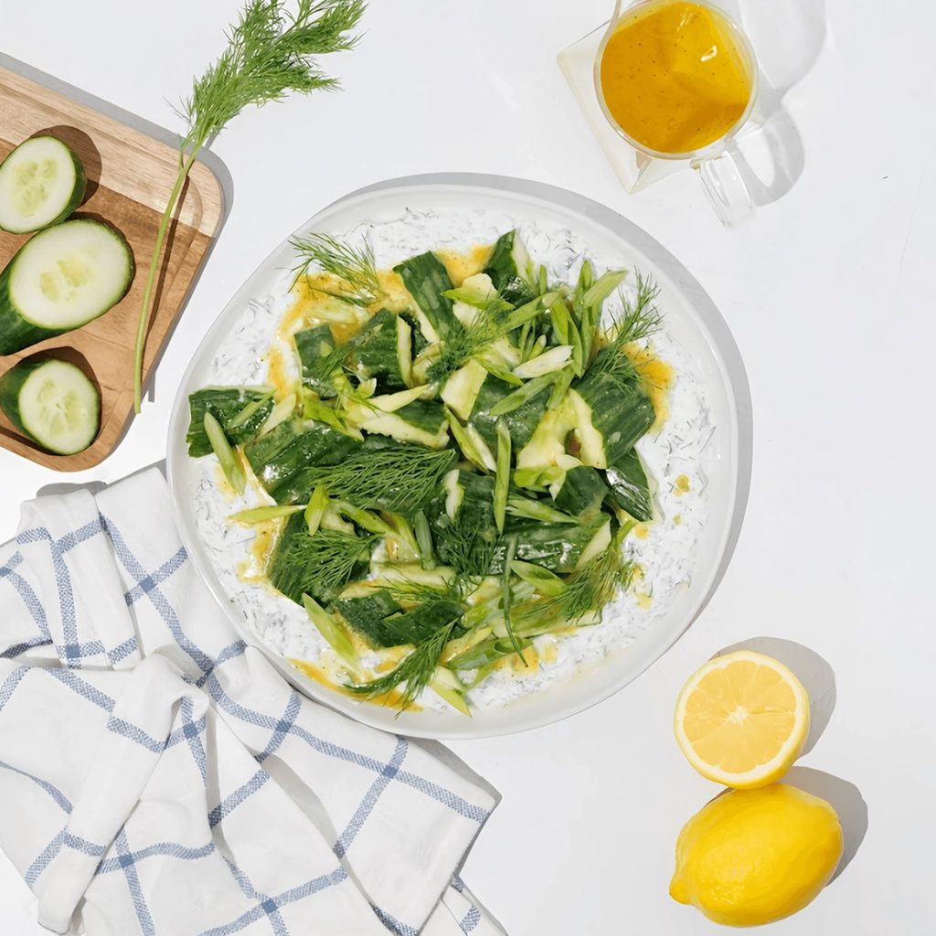 Cucumber salad with dill and yellow dressing on a yogurt-covered plate, with lemon and sliced cucumber.