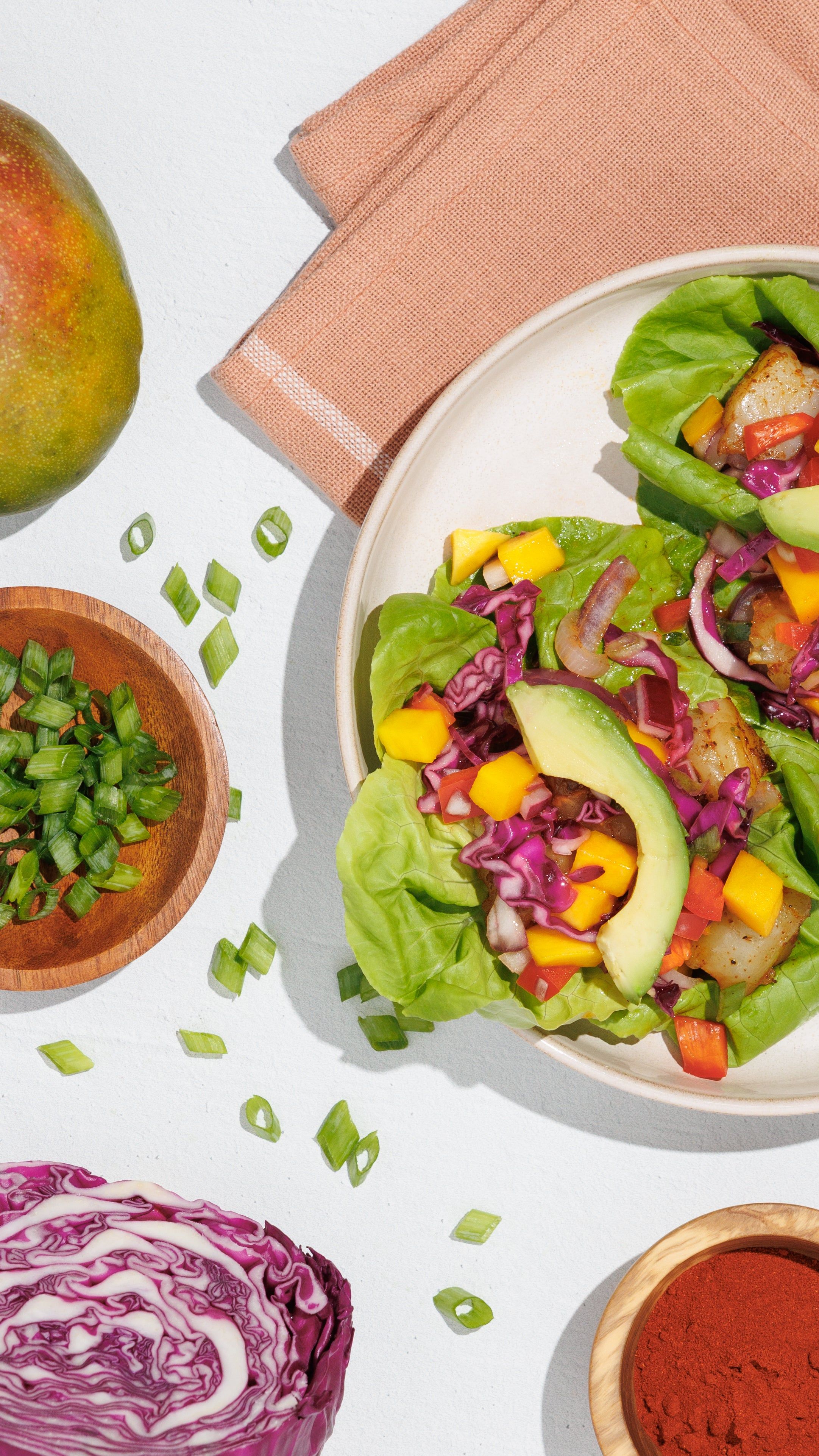 Shrimp lettuce tacos with avocado, mango, red cabbage, and peppers on a white table.
