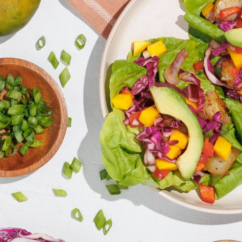 Shrimp lettuce tacos with avocado, mango, red cabbage, and peppers on a white table.