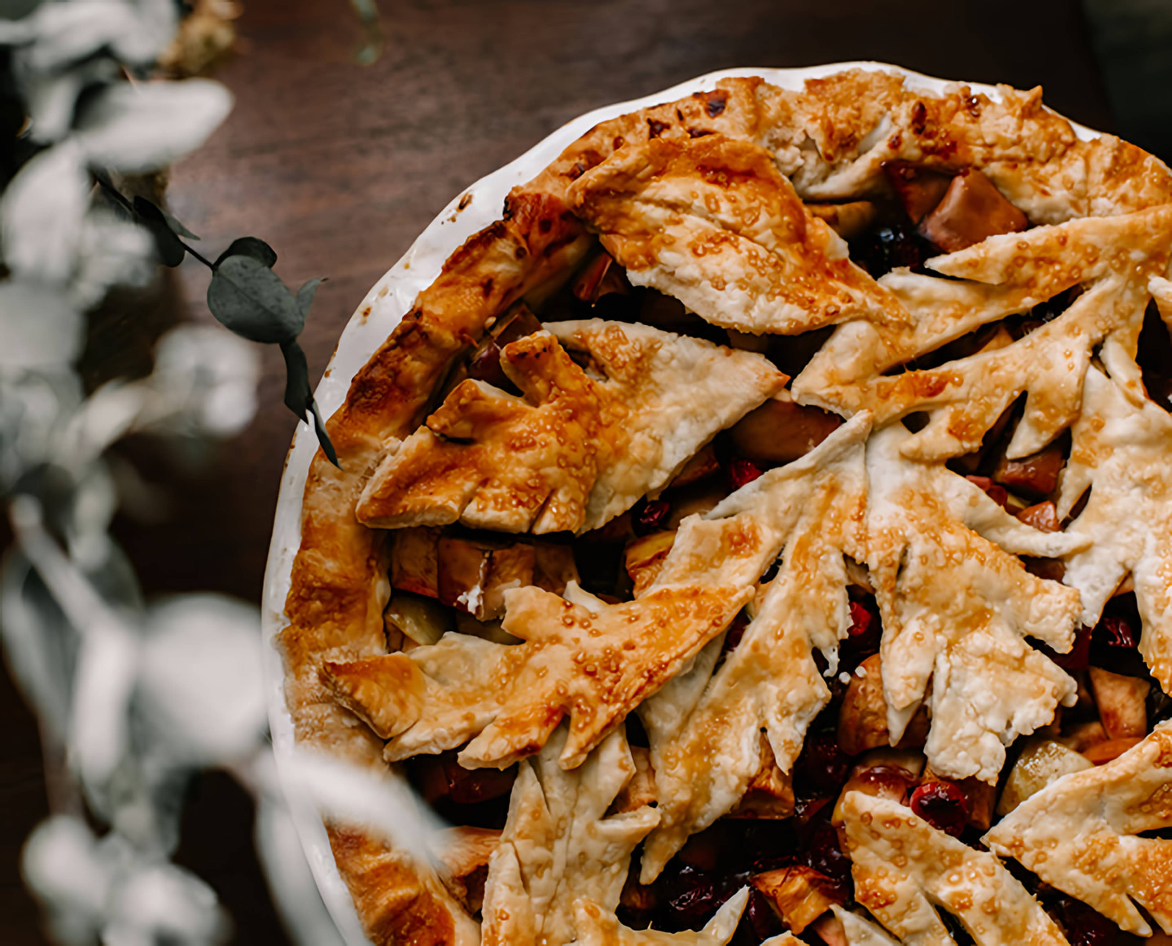 Overhead view of a golden lattice-topped fruit pie in a white dish on a dark table.