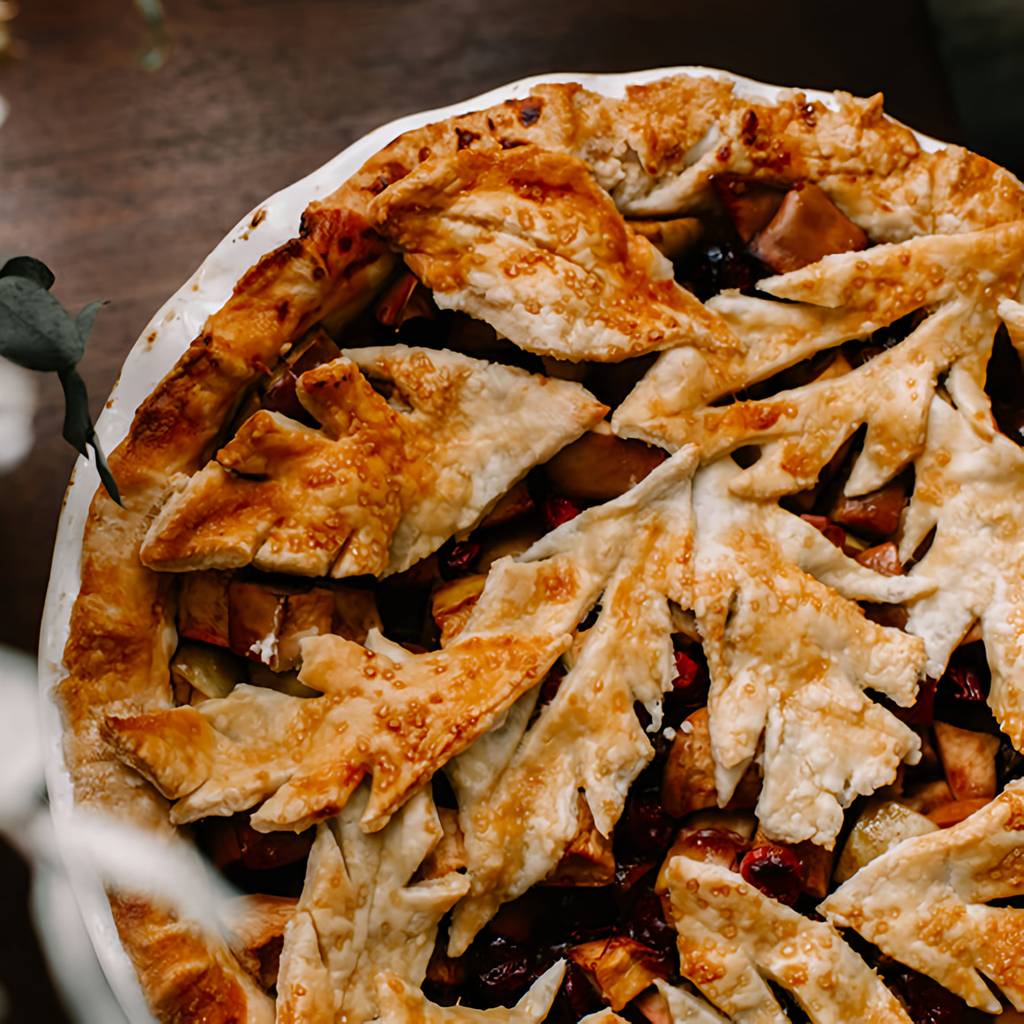 Overhead view of a golden lattice-topped fruit pie in a white dish on a dark table.