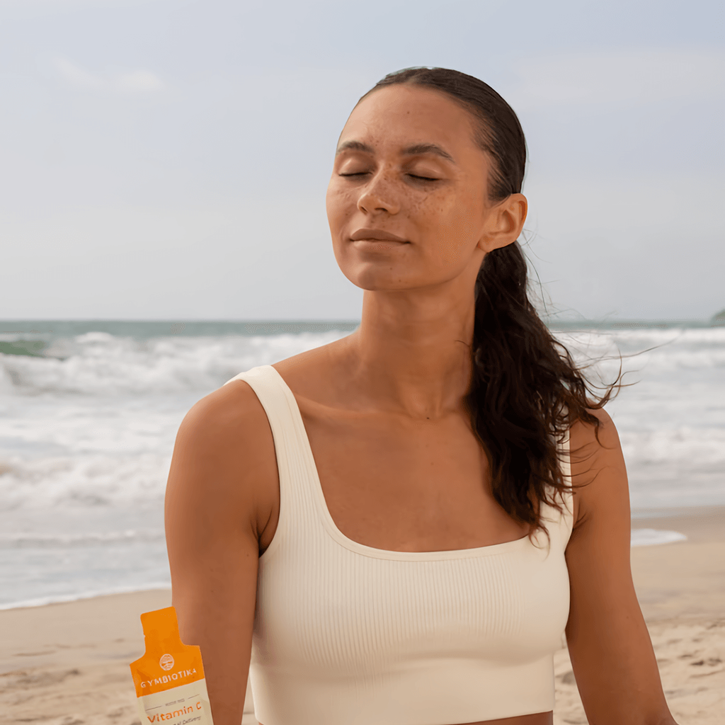 A woman sits on a beach with her eyes closed, holding an orange Vitamin C packet.