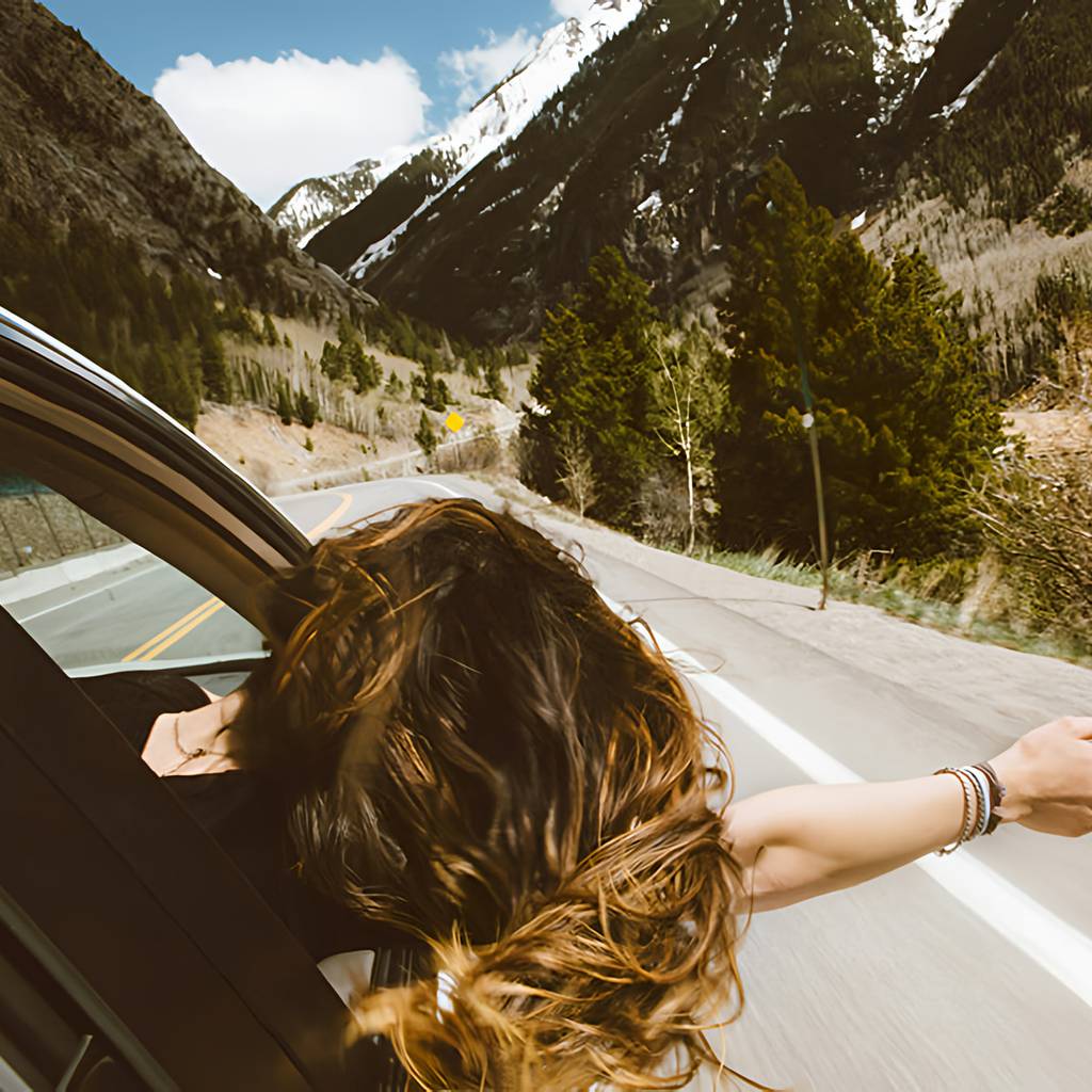 Person with long hair leans out of a car window on a mountain road.