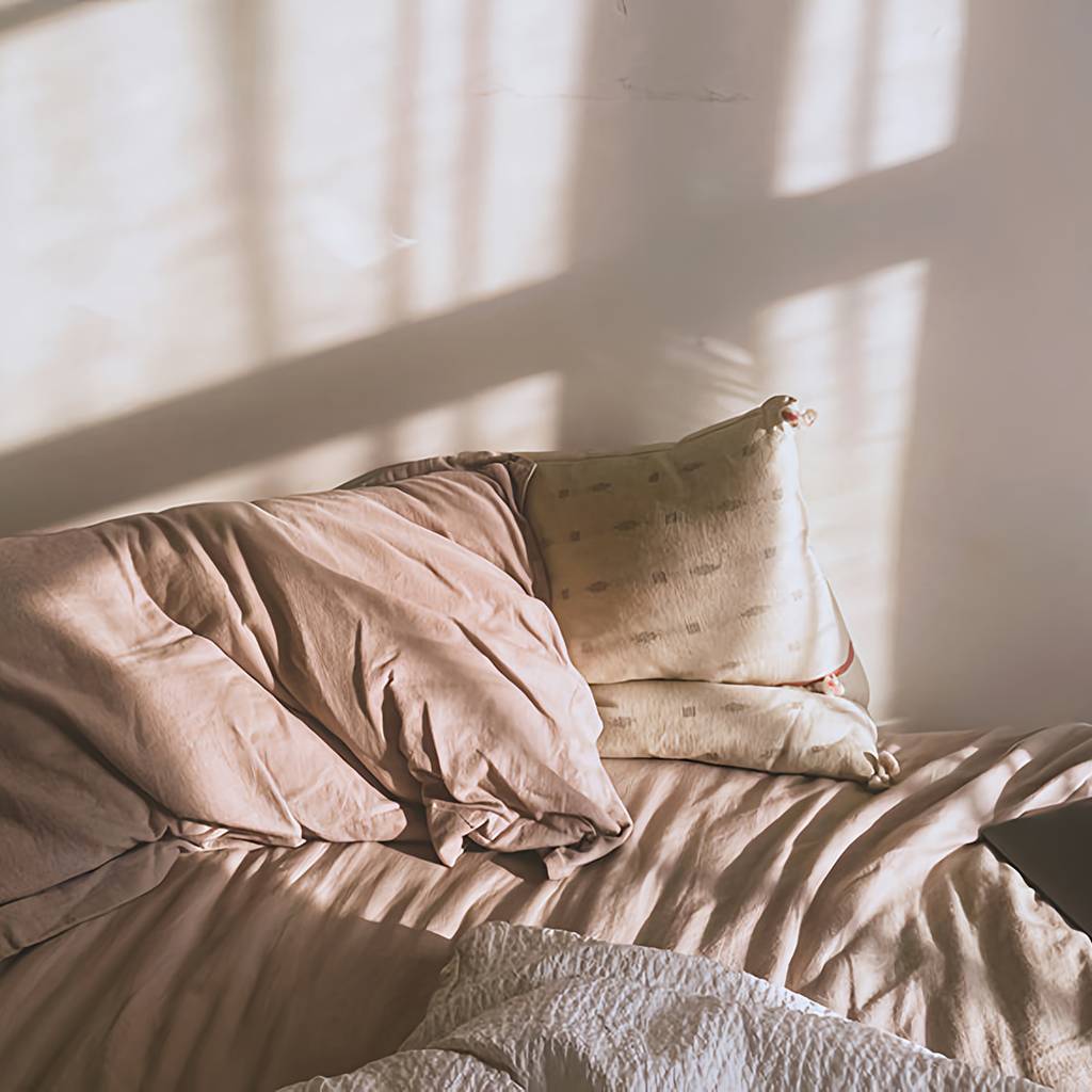 Unmade bed with rumpled pillows, a white blanket, and a closed laptop in window light.