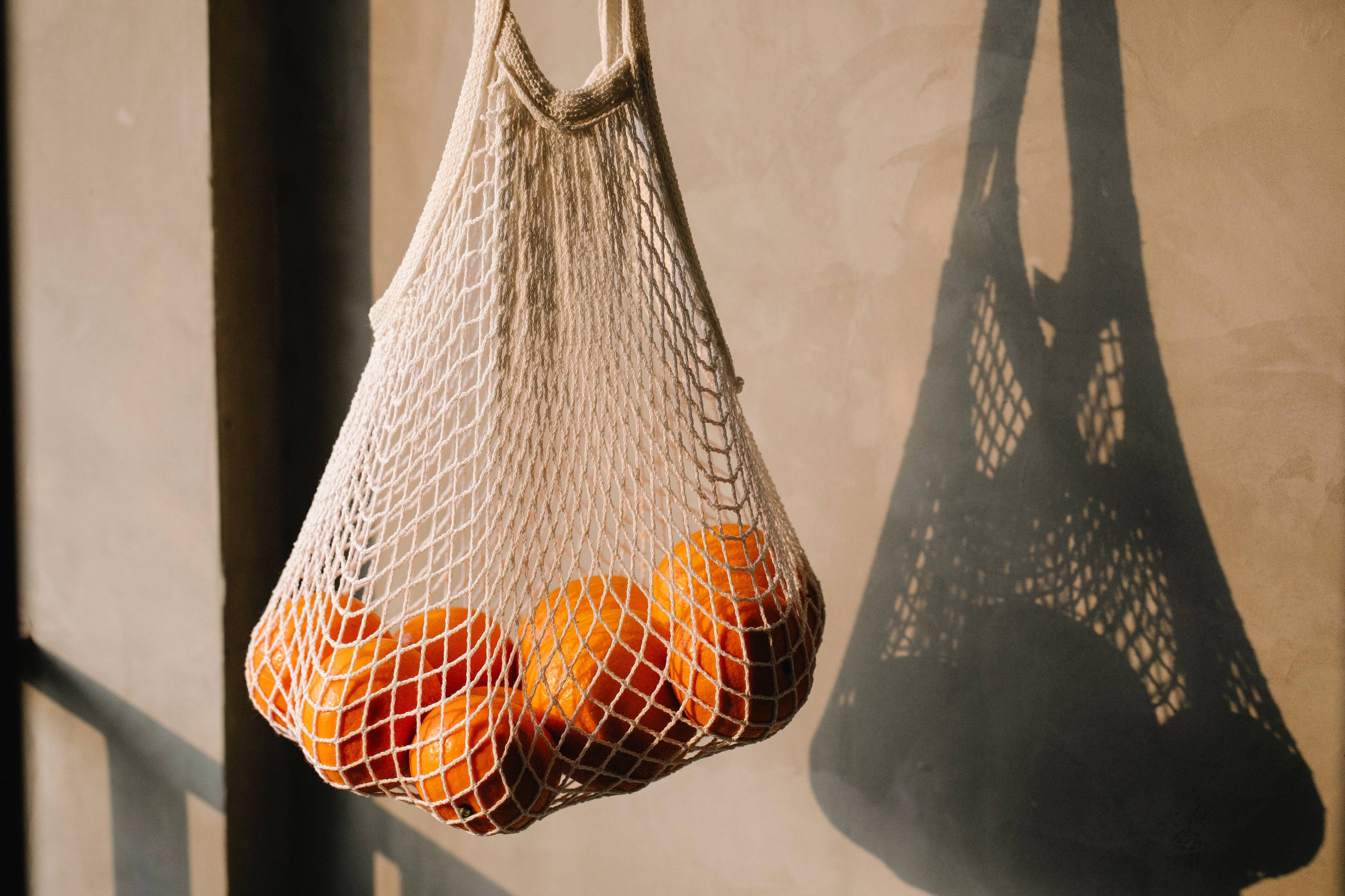 A mesh bag filled with oranges hangs in sunlight.
