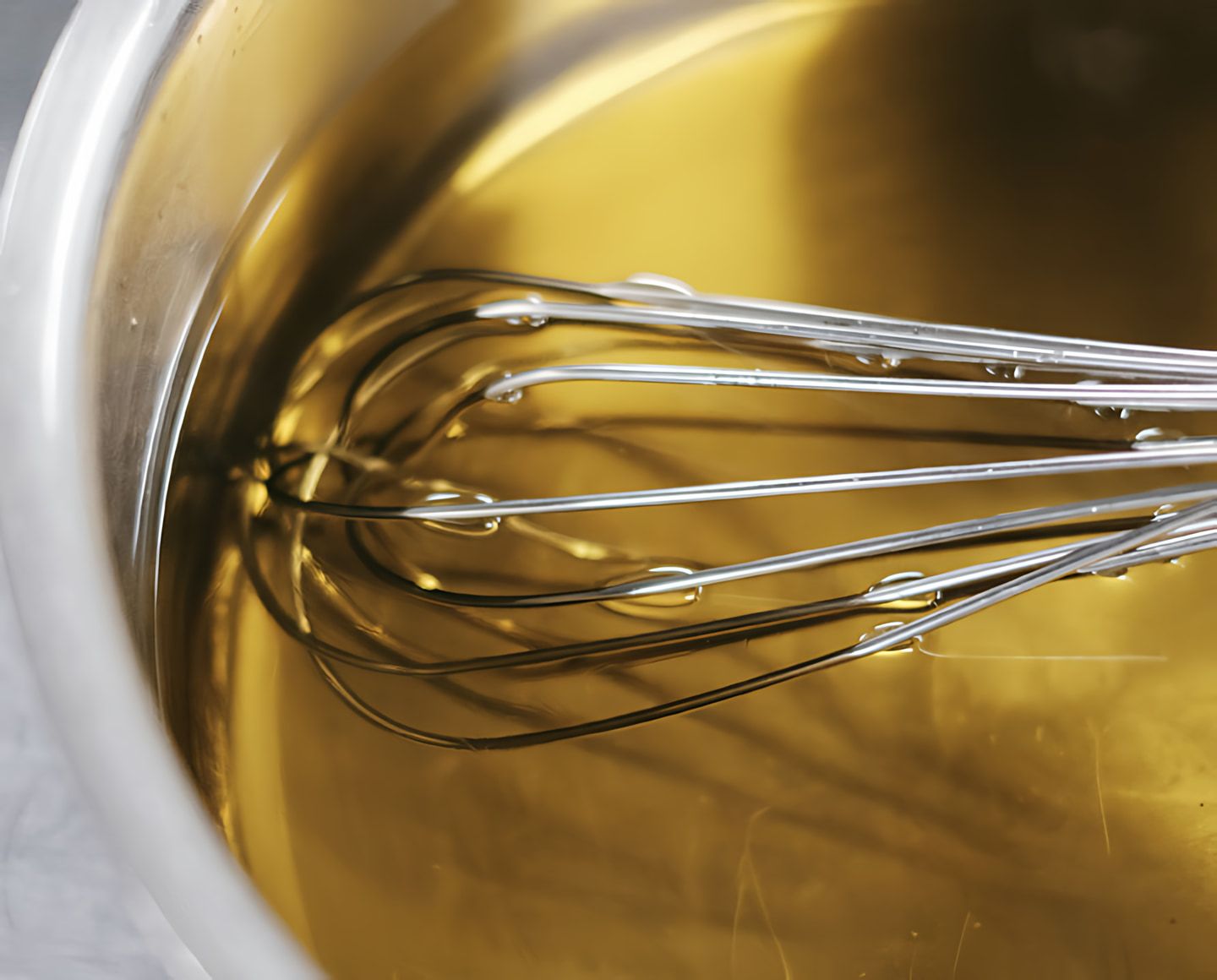 A whisk in a bowl of golden liquid