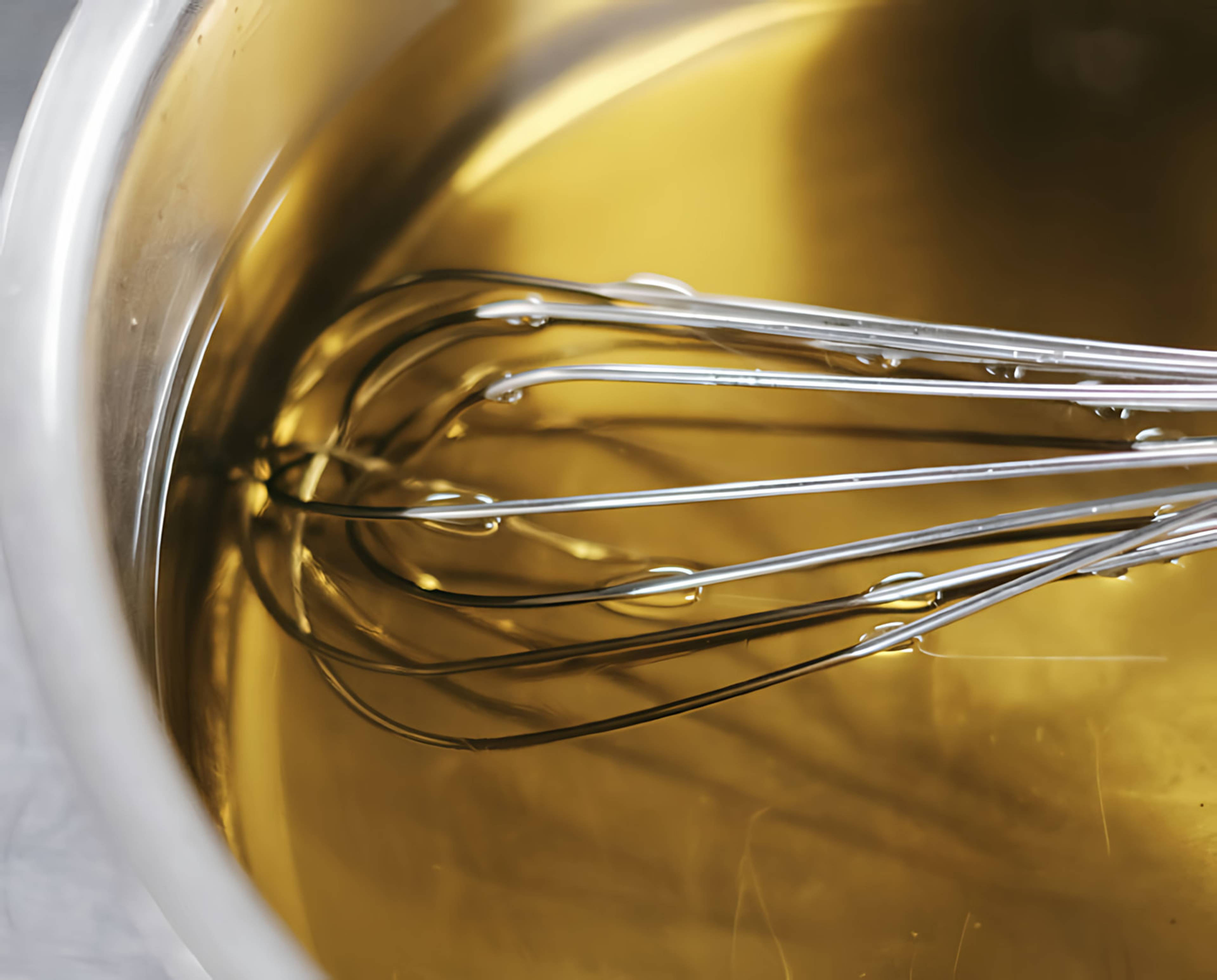 A whisk in a bowl of golden liquid