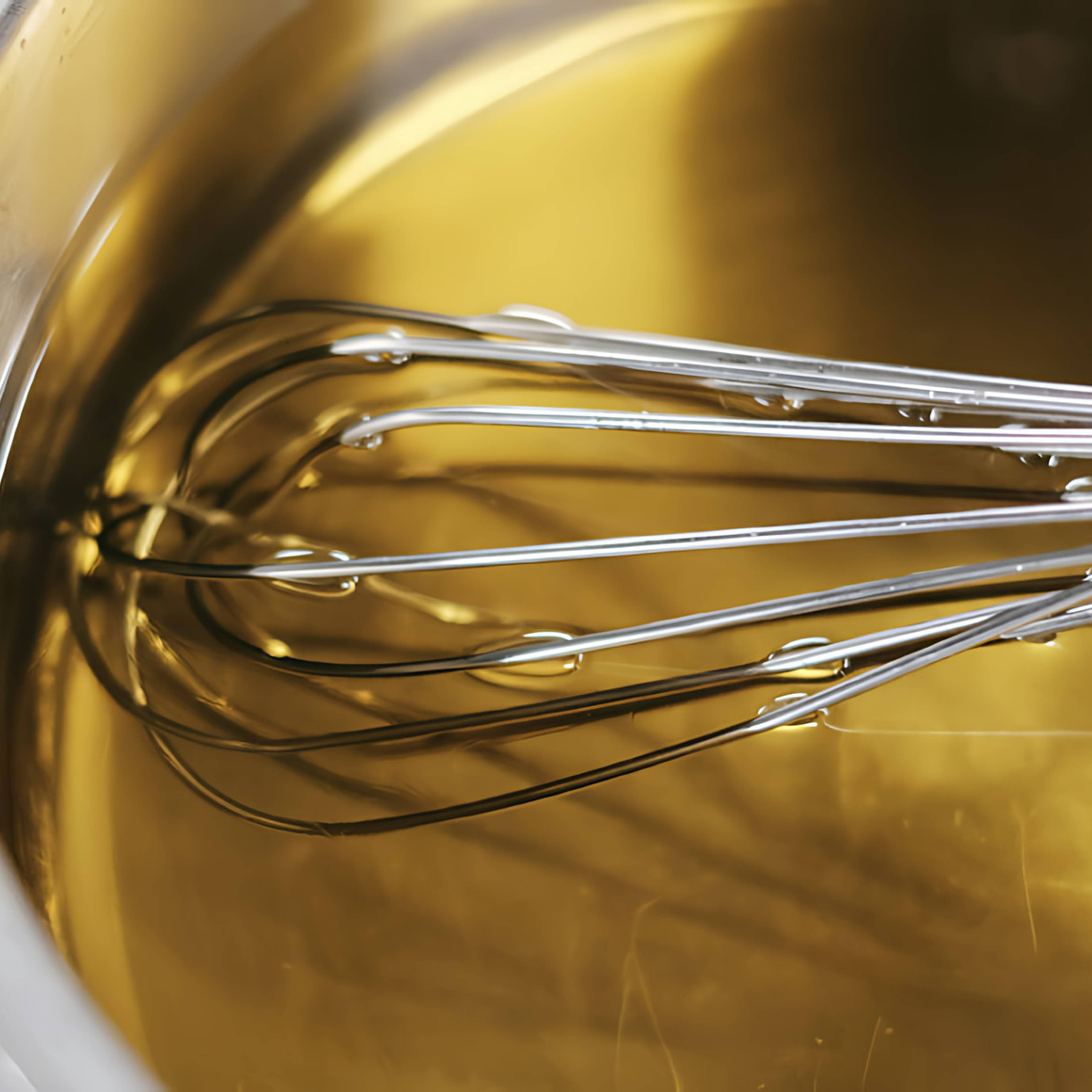A whisk in a bowl of golden liquid