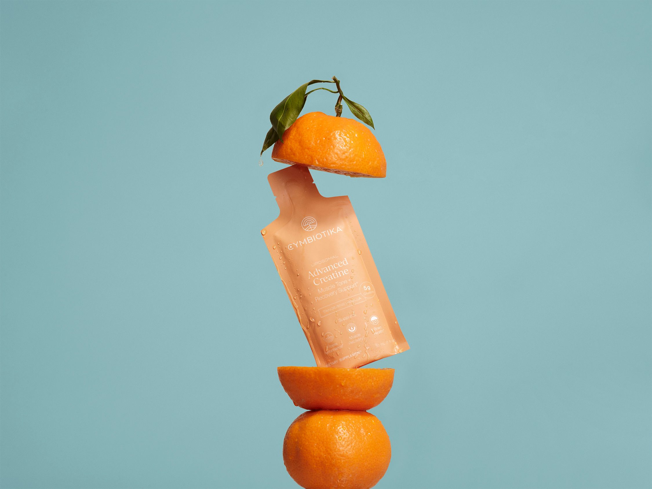 Orange Advanced Creatine sachet suspended between orange halves against a blue background.